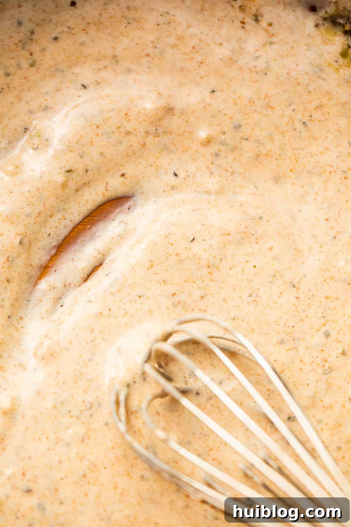 Vibrant Fiesta Pasta Medley 5 A whisk stirring a creamy, light yellow dressing in a clear glass bowl.