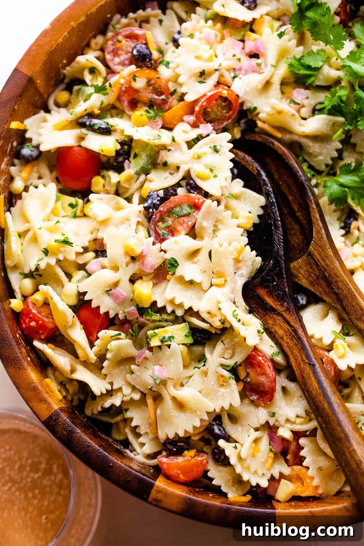 Vibrant Fiesta Pasta Medley 6 Fiesta Pasta Salad in a wooden serving bowl, garnished with fresh cilantro, with serving spoons ready.