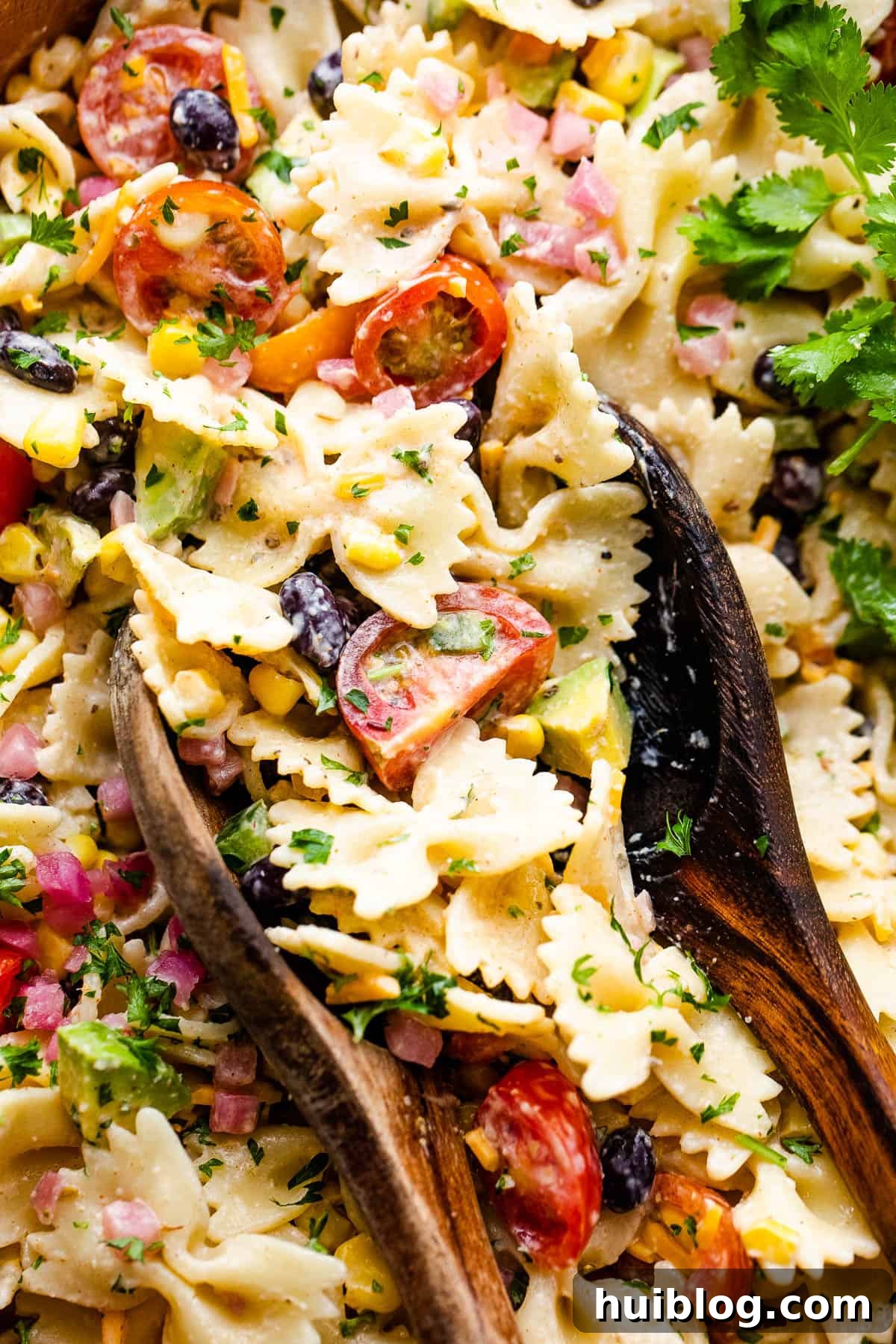 Vibrant Fiesta Pasta Medley 7 Close-up of Fiesta Pasta Salad in a wooden bowl, ready for serving with two wooden spoons.