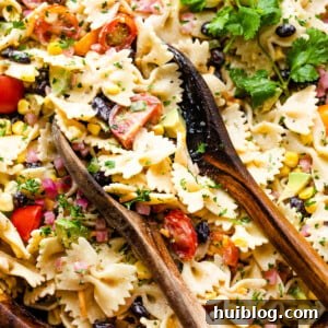A large wooden salad bowl filled with colorful Fiesta Pasta Salad, garnished with fresh cilantro, with two wooden serving spoons.