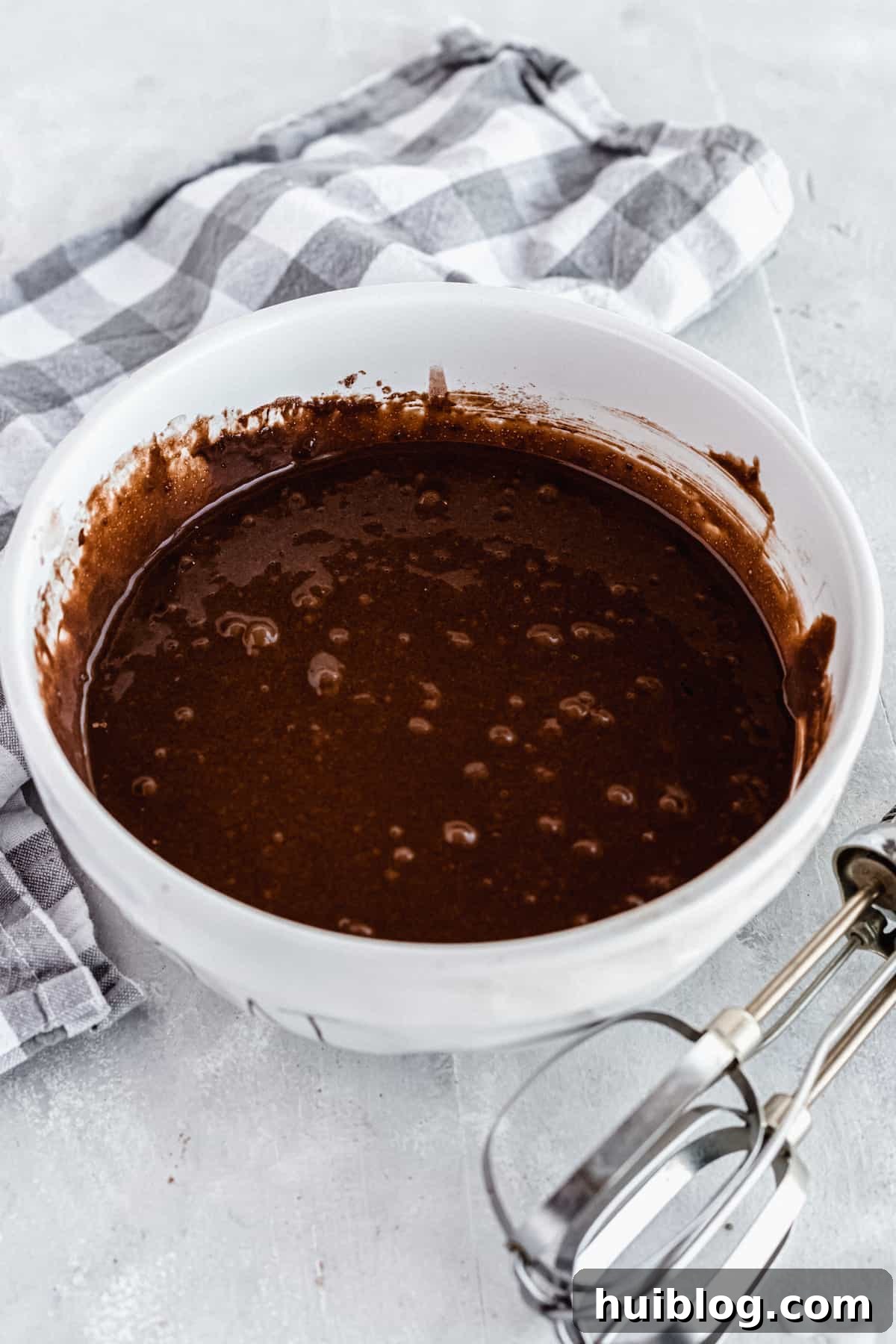 A white bowl filled with smooth cake batter next to a metal whisk