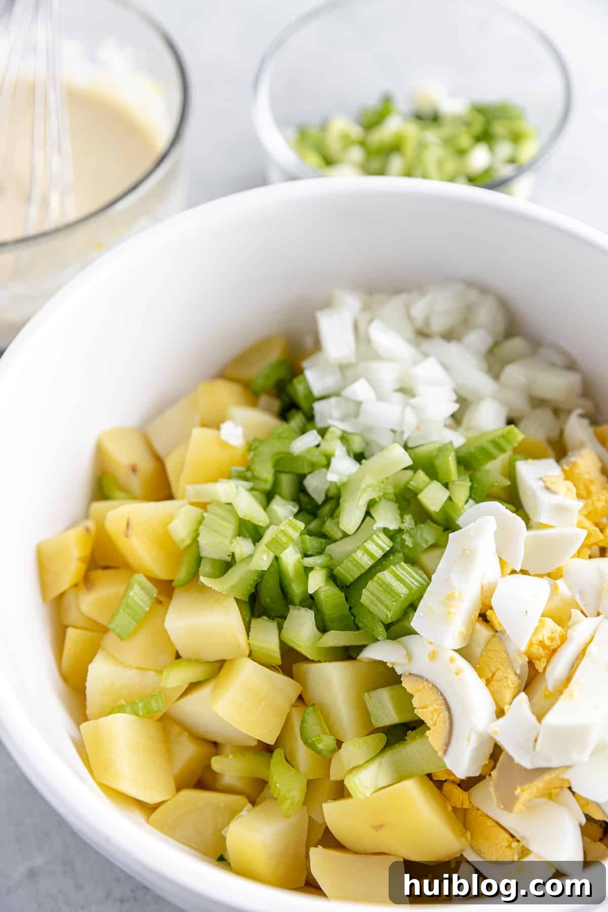 All-American Potato Salad 5 A White Bowl Filled with Uncombined Potato Salad Ingredients: potatoes, celery, onion, and hard-boiled eggs.