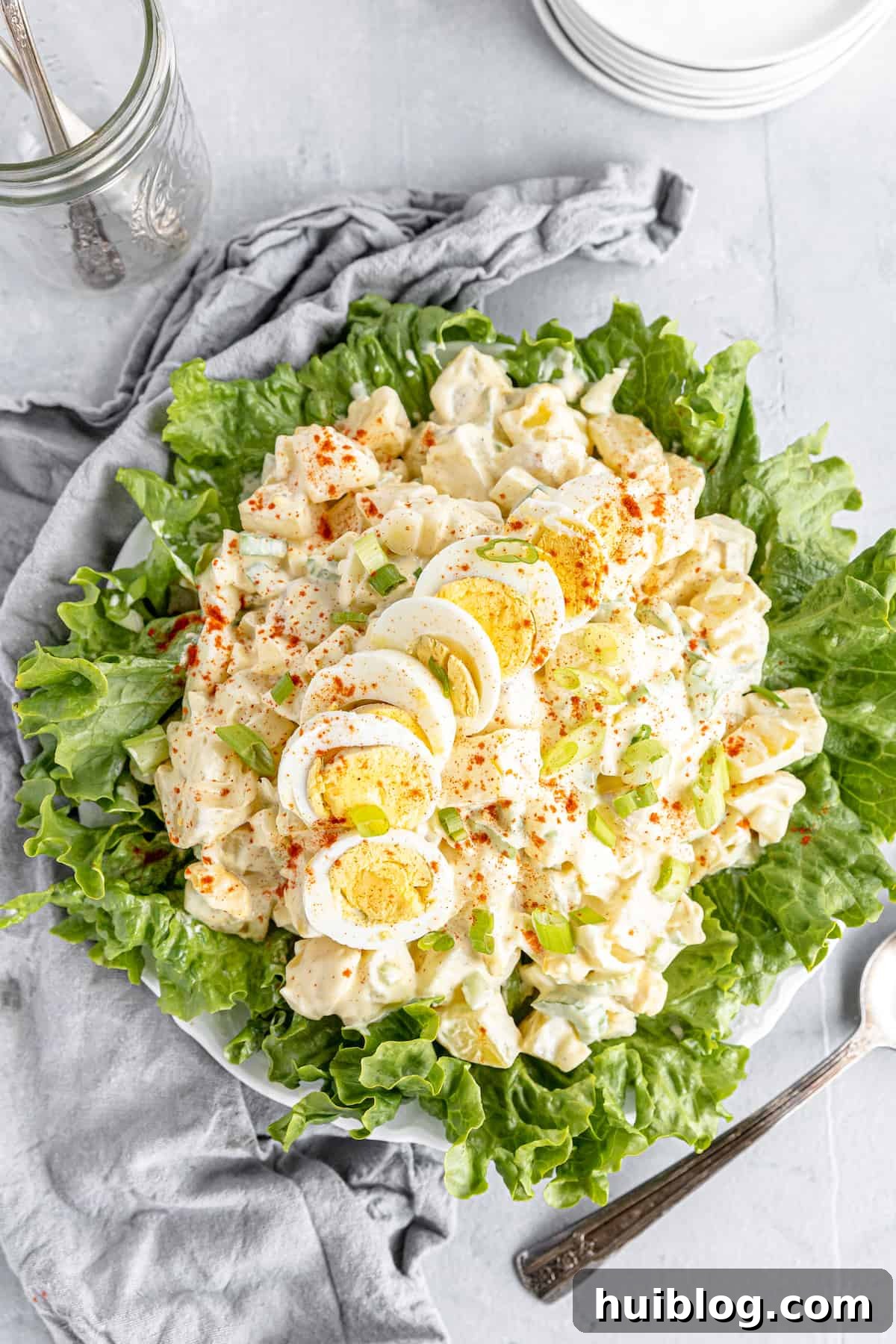 All-American Potato Salad 9 An Overhead Shot of a Potato Salad on a Lettuce-Lined Plate Beside a Gray Kitchen Towel, emphasizing its homemade appeal.
