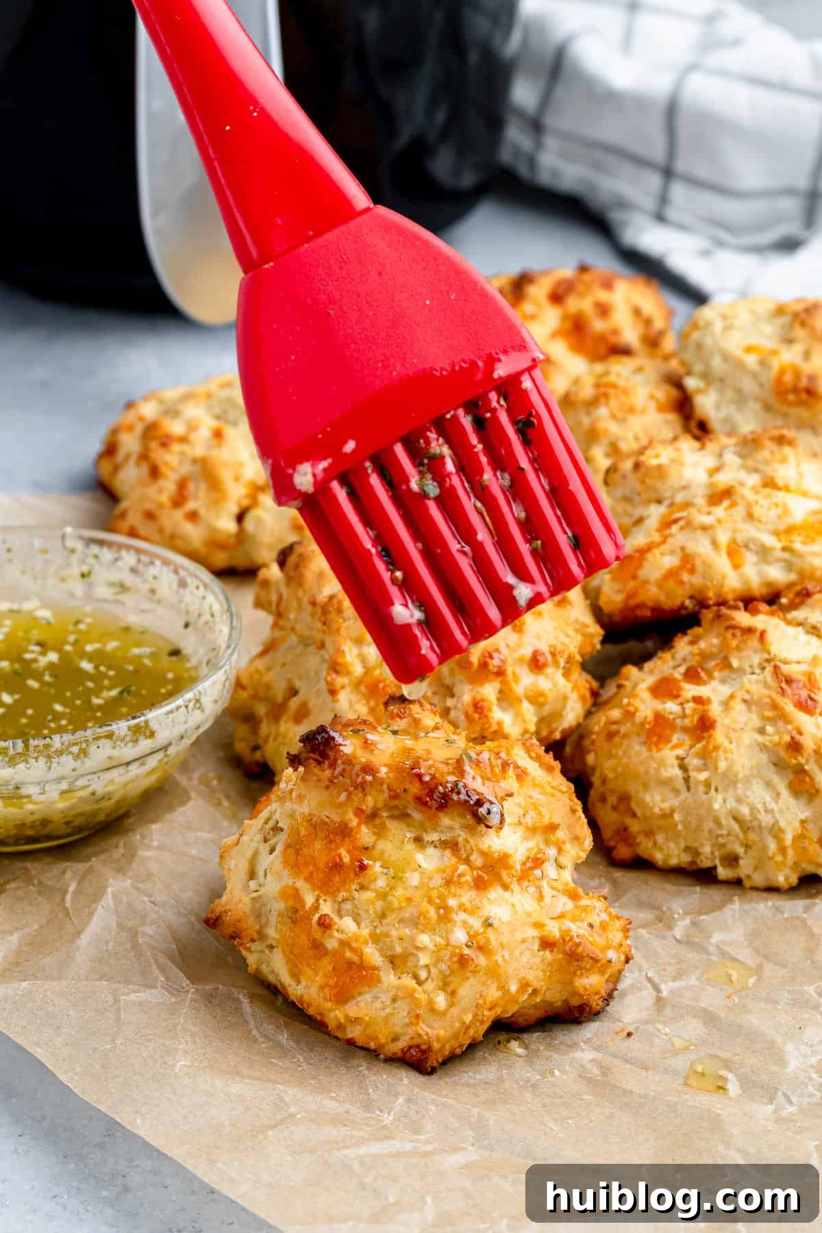 Garlic butter being brushed over an air fryer biscuit with a red pastry brush