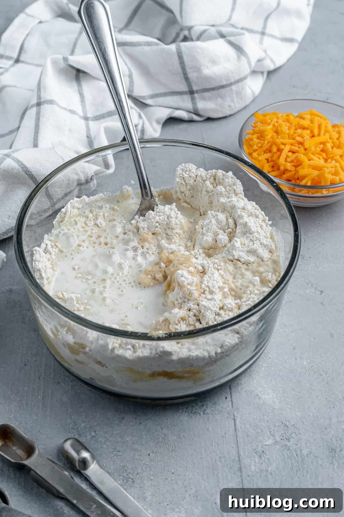 Bisquick mix, milk, and butter in a bowl beside a dish of shredded cheddar