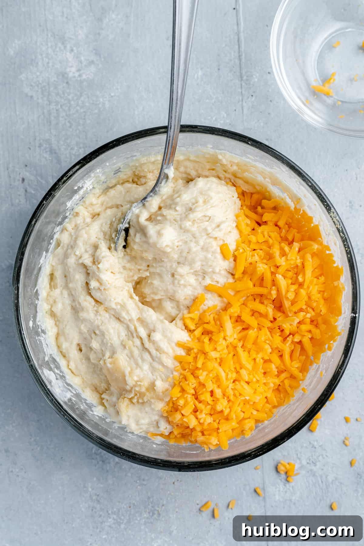 Shredded cheddar cheese being mixed into the biscuit batter with a spoon
