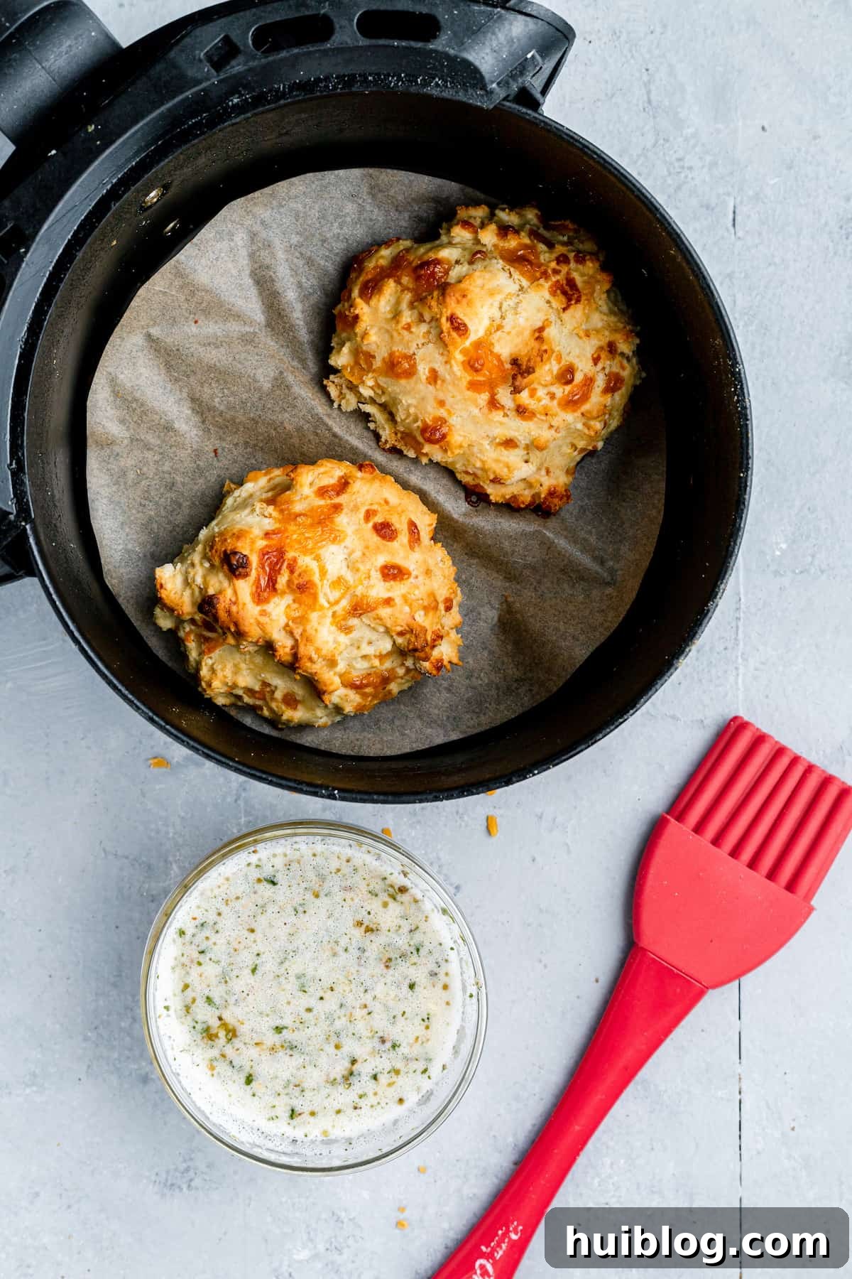 Two Red Lobster biscuits in an air fryer beside a dish of garlic butter
