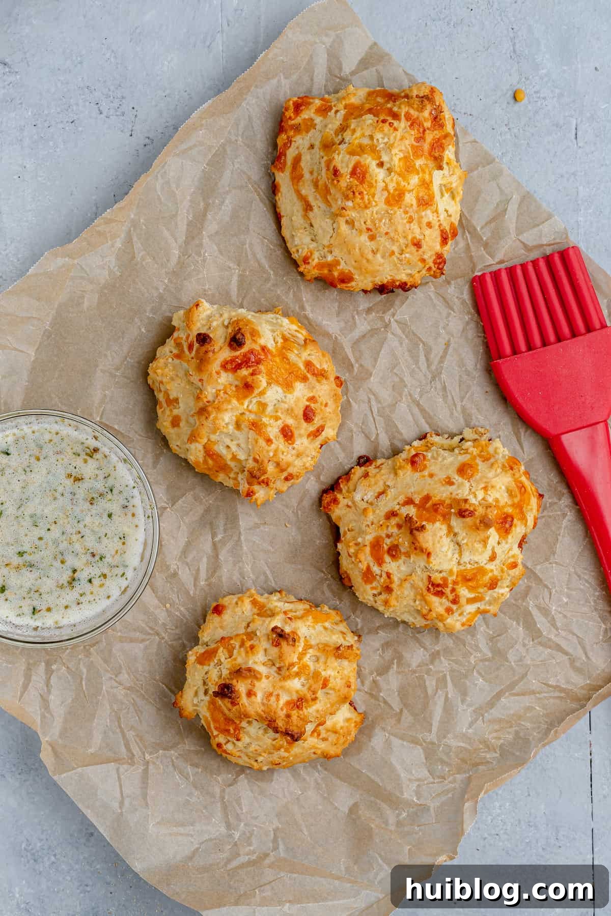 Four air fryer biscuits on a sheet of parchment paper with a pastry brush and a small dish of garlic butter