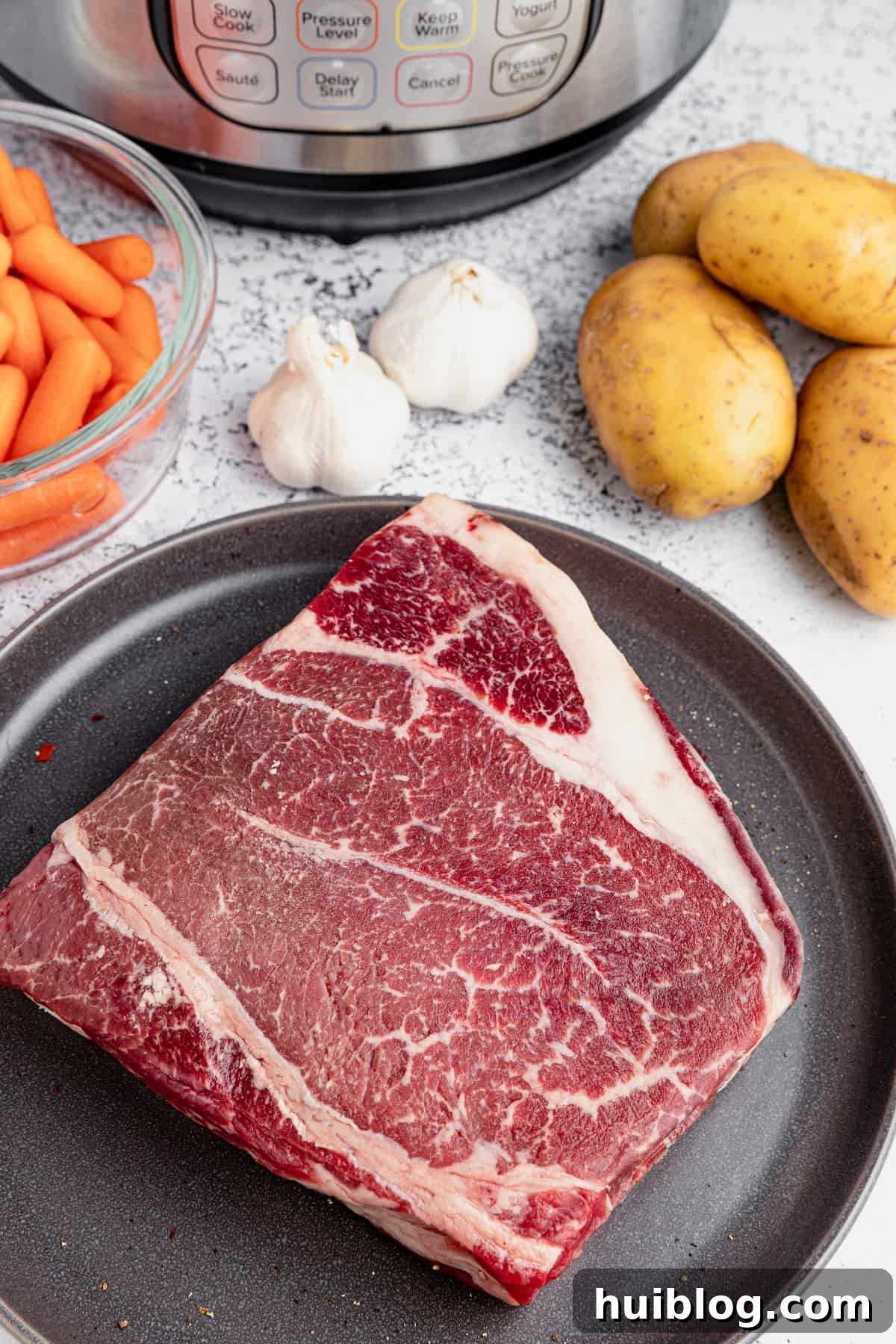 Fork-Tender Instant Pot Pot Roast with Carrots and Potatoes 3 Seasoned beef roast, potatoes, garlic cloves, and carrots on a cutting board.