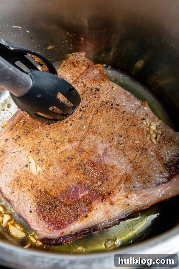 Fork-Tender Instant Pot Pot Roast with Carrots and Potatoes 5 Beef roast being browned in an Instant Pot with tongs.