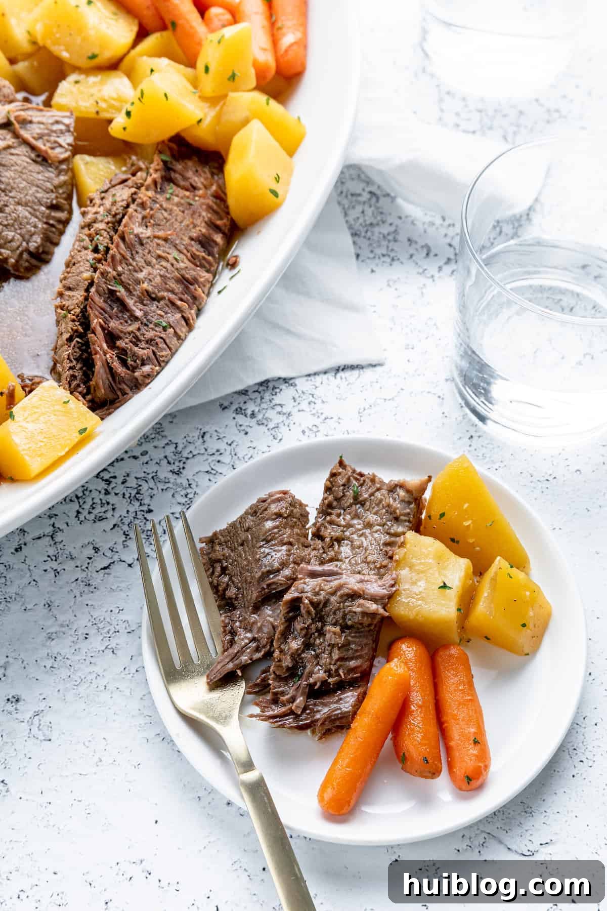Fork-Tender Instant Pot Pot Roast with Carrots and Potatoes 8 A white plate with a generous serving of pot roast, carrots, and potatoes, garnished with fresh herbs.