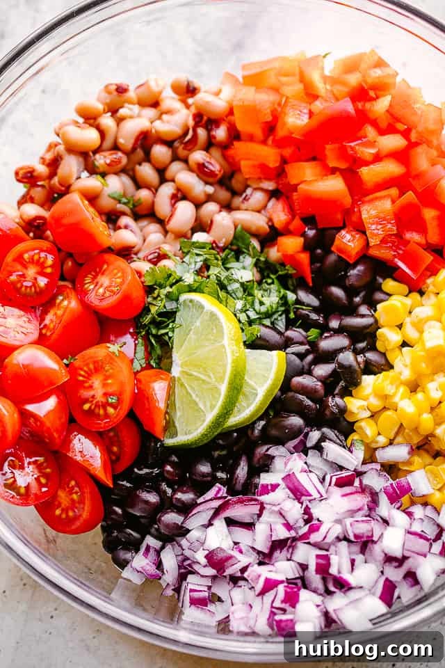 avocado, corn, tomatoes, black-eyed peas, beans and cilantro in a large glass bowl, ingredients ready to mix