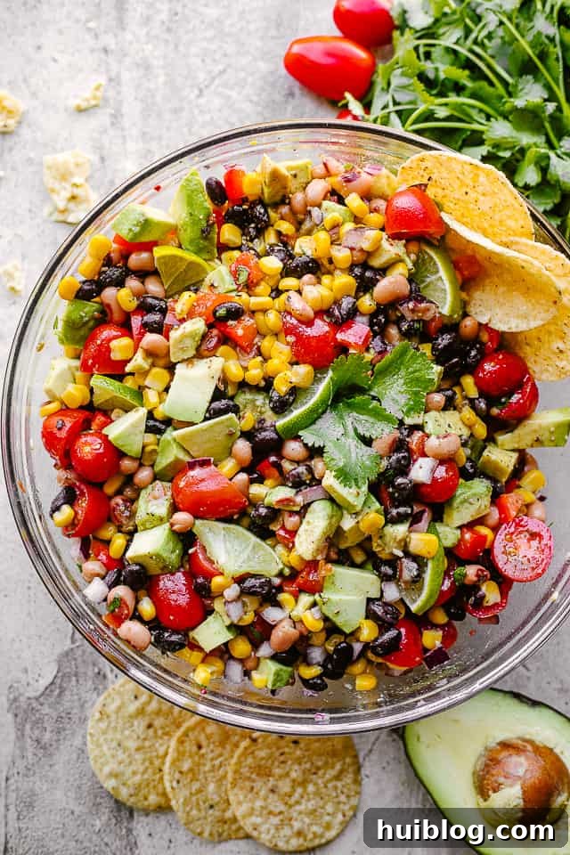 Cowboy caviar with avocado, corn, tomatoes, black-eyed peas, beans and cilantro in a large glass bowl, ready to serve