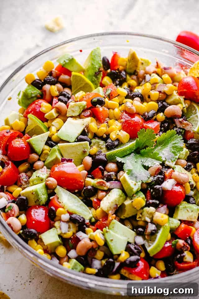 avocado, corn, tomatoes, black-eyed peas, beans and cilantro in a large glass bowl, close up from the side