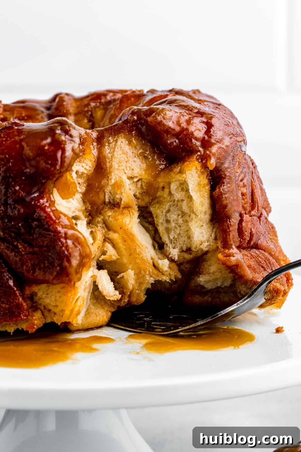 Gooey Cinnamon Pull-Apart Treat 6 A baked monkey bread, golden and glistening, displayed on a cake stand with a few pieces already removed, and a cake server ready for more.