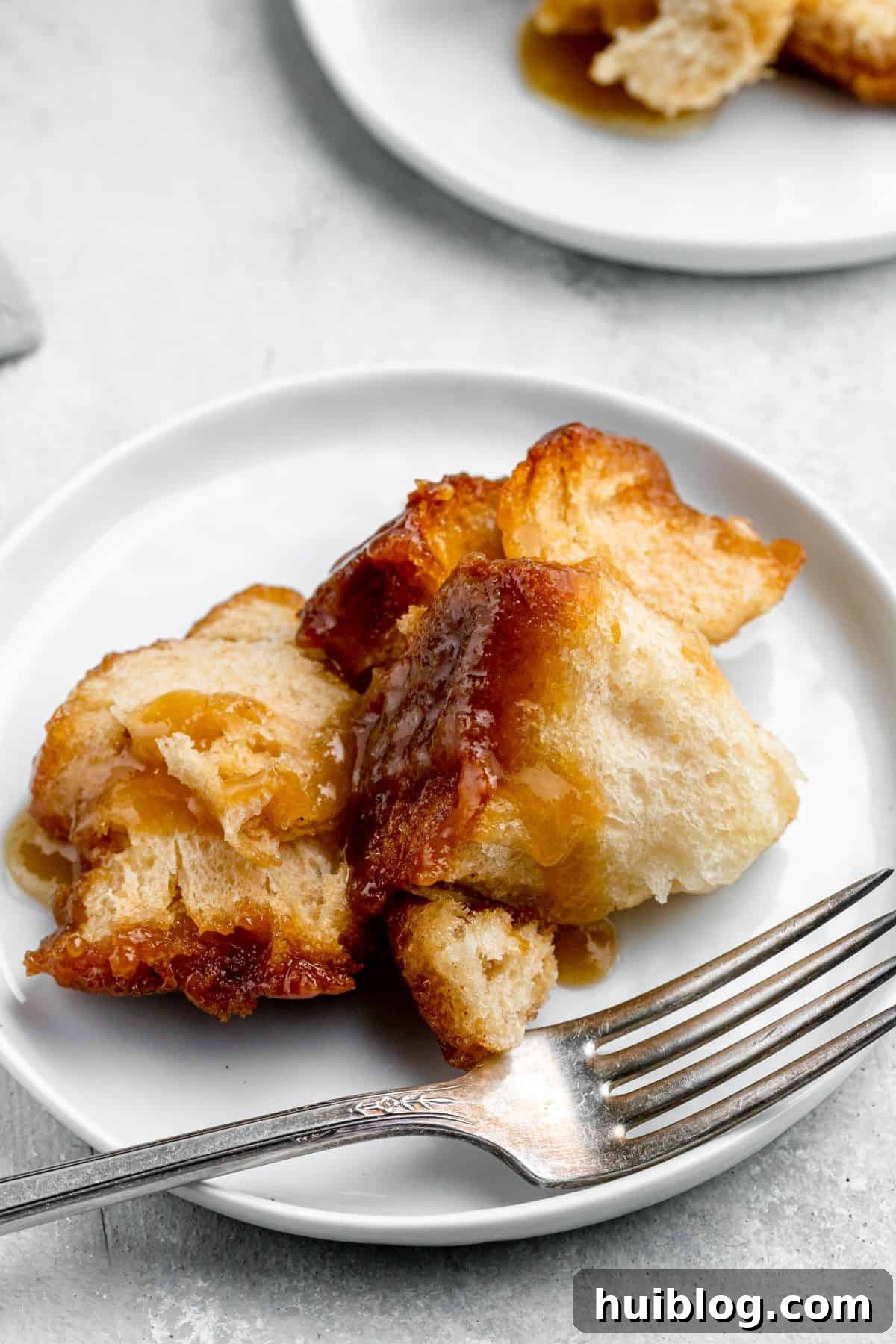 Gooey Cinnamon Pull-Apart Treat 7 A generous serving of monkey bread on a white dessert plate with a fork, ready to be enjoyed.