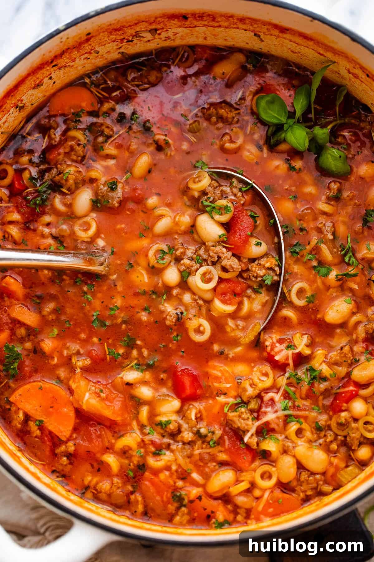 A bowl of Pasta Fagioli soup in a white Dutch oven with a ladle, ready to be served.