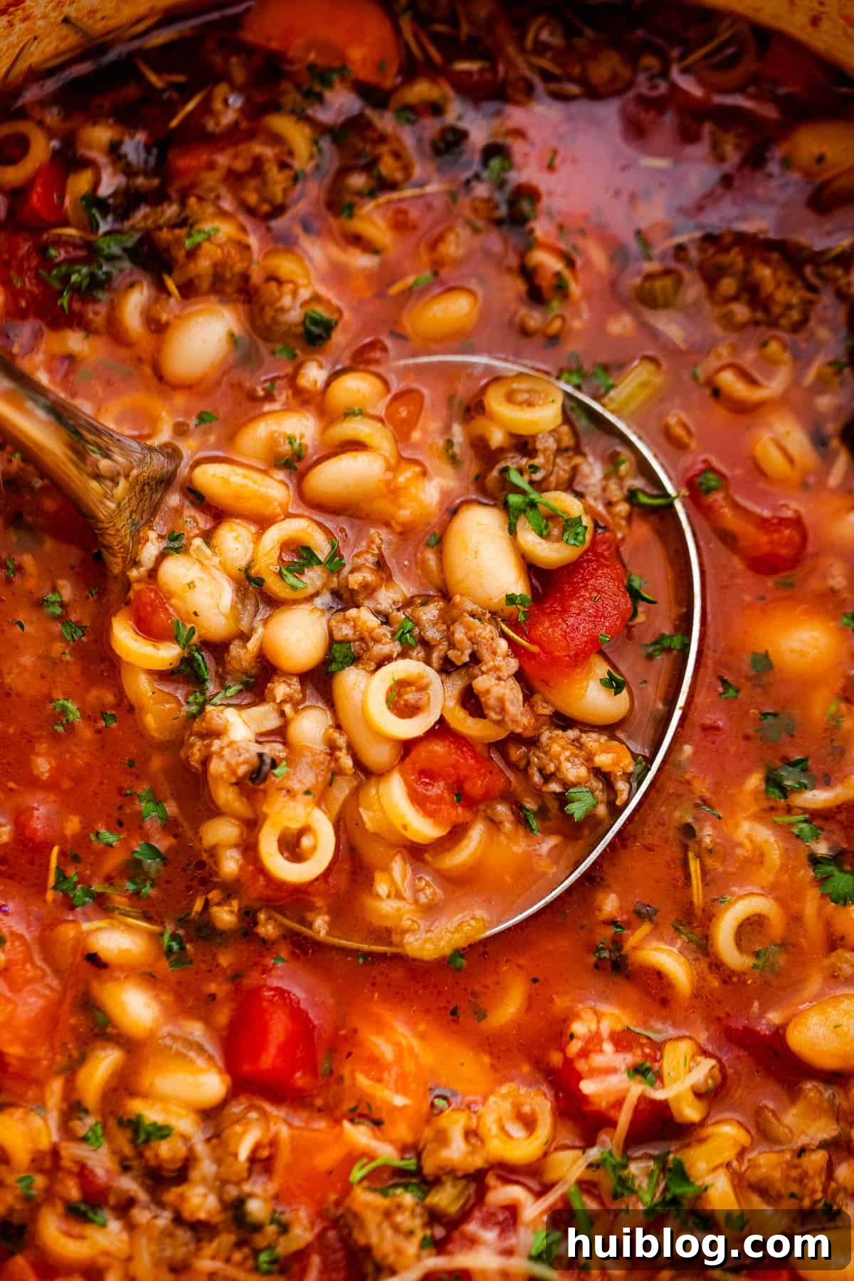 Close-up shot of a ladle scooping out Pasta Fagioli soup from a white Dutch oven.