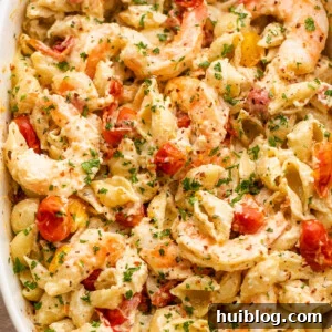 white baking dish with shrimp and pasta tossed with a cream cheese sauce and cherry tomatoes