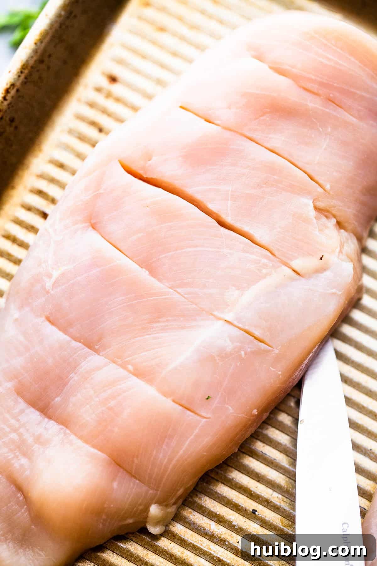raw chicken breasts cut hasselback style, showing the slits prepared for stuffing