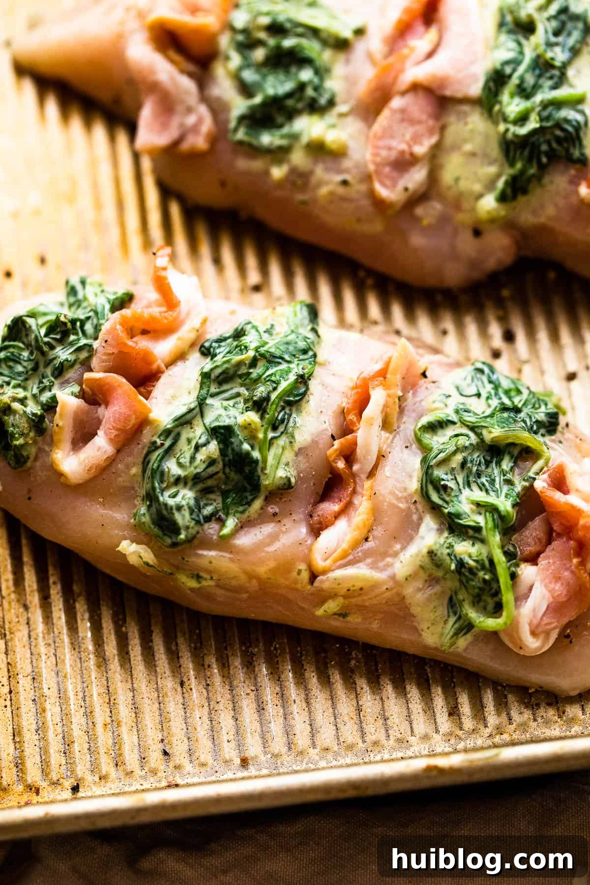 raw chicken breasts cut hasselback style and stuffed with creamed spinach plus bacon, ready for baking