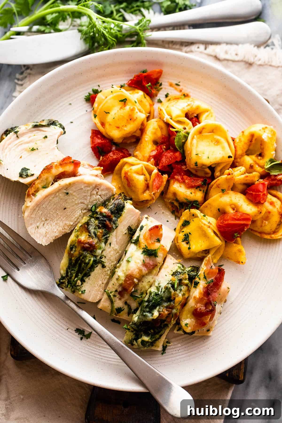 cut up stuffed chicken breast served alongside tortellini pasta, highlighting the textures of the chicken and filling