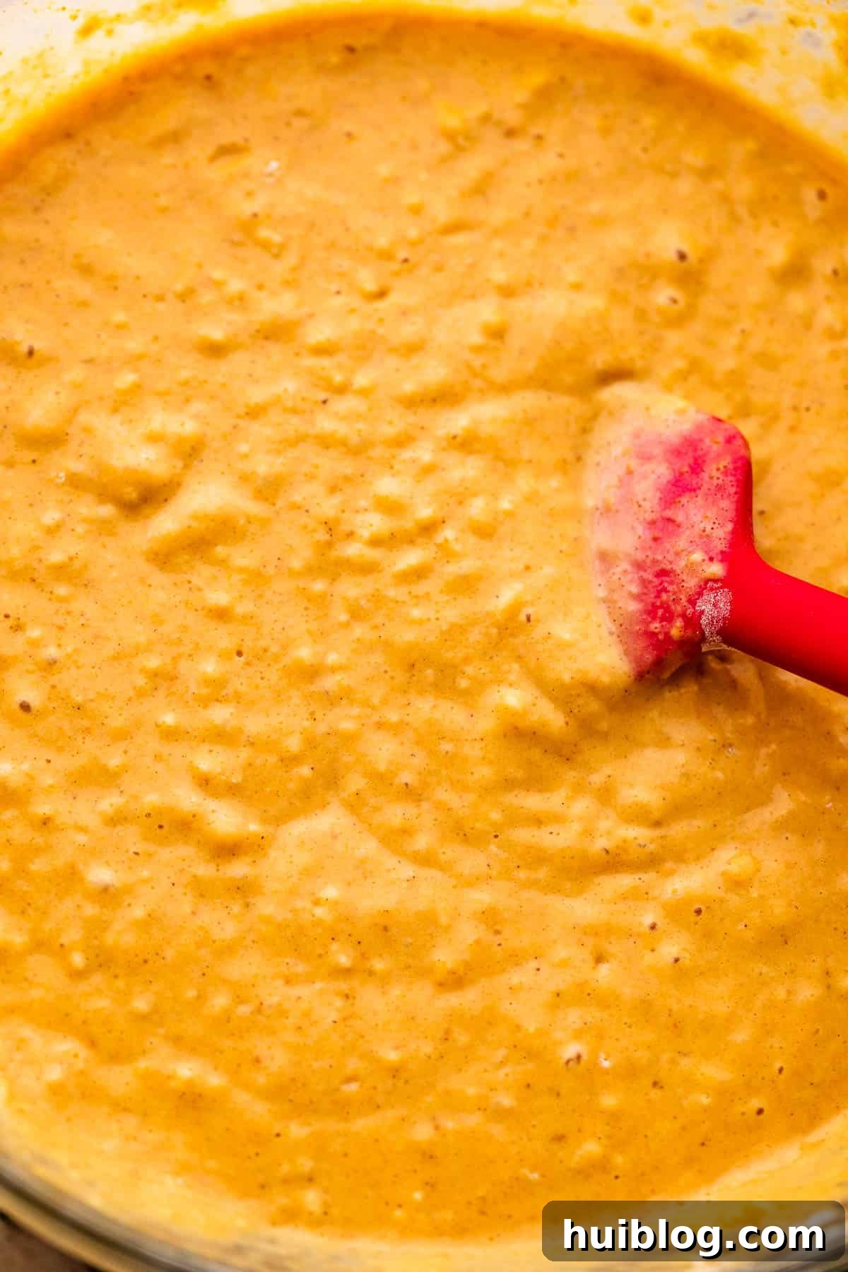 Close-up of a hand gently stirring vibrant orange pumpkin pancake batter in a mixing bowl.