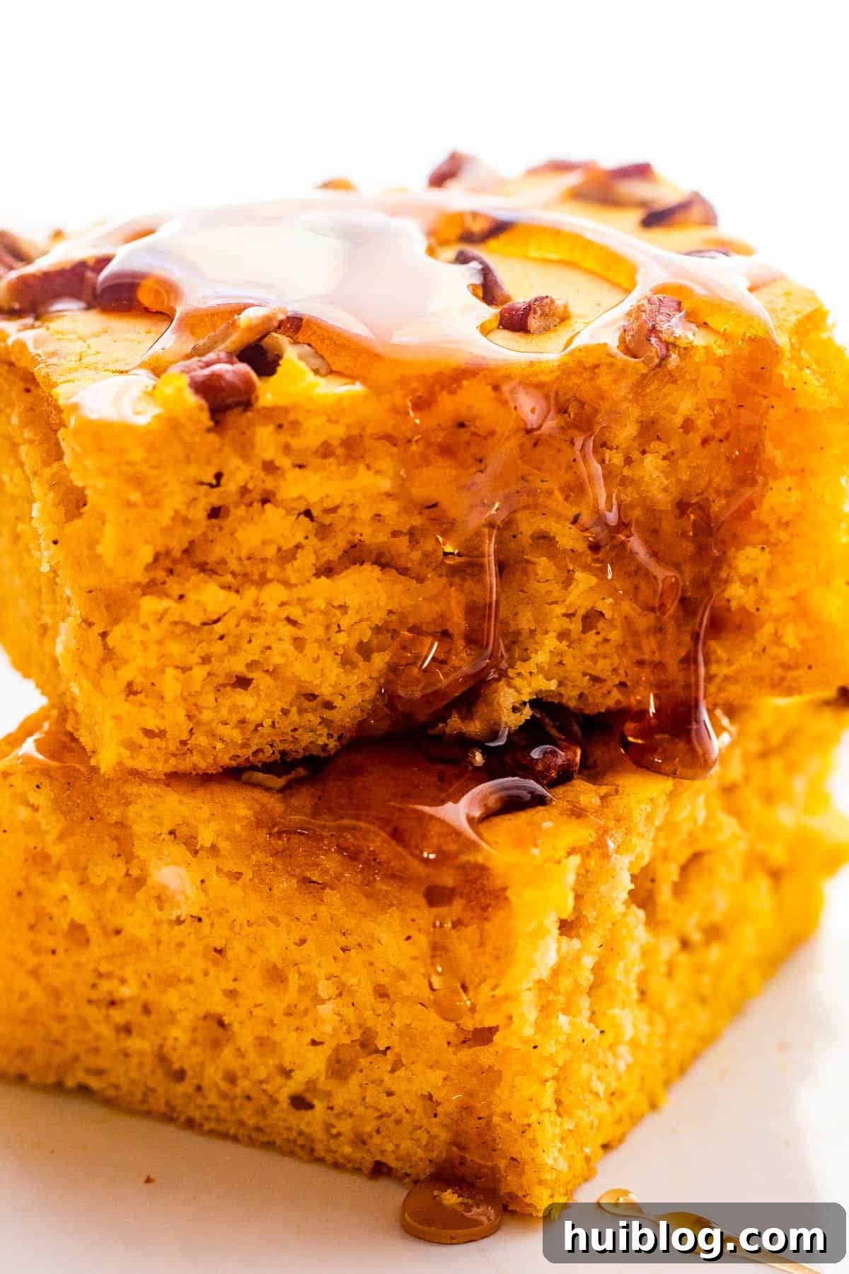 Two fluffy sheet pan pumpkin pancakes stacked on top of each other, drizzled with maple syrup.
