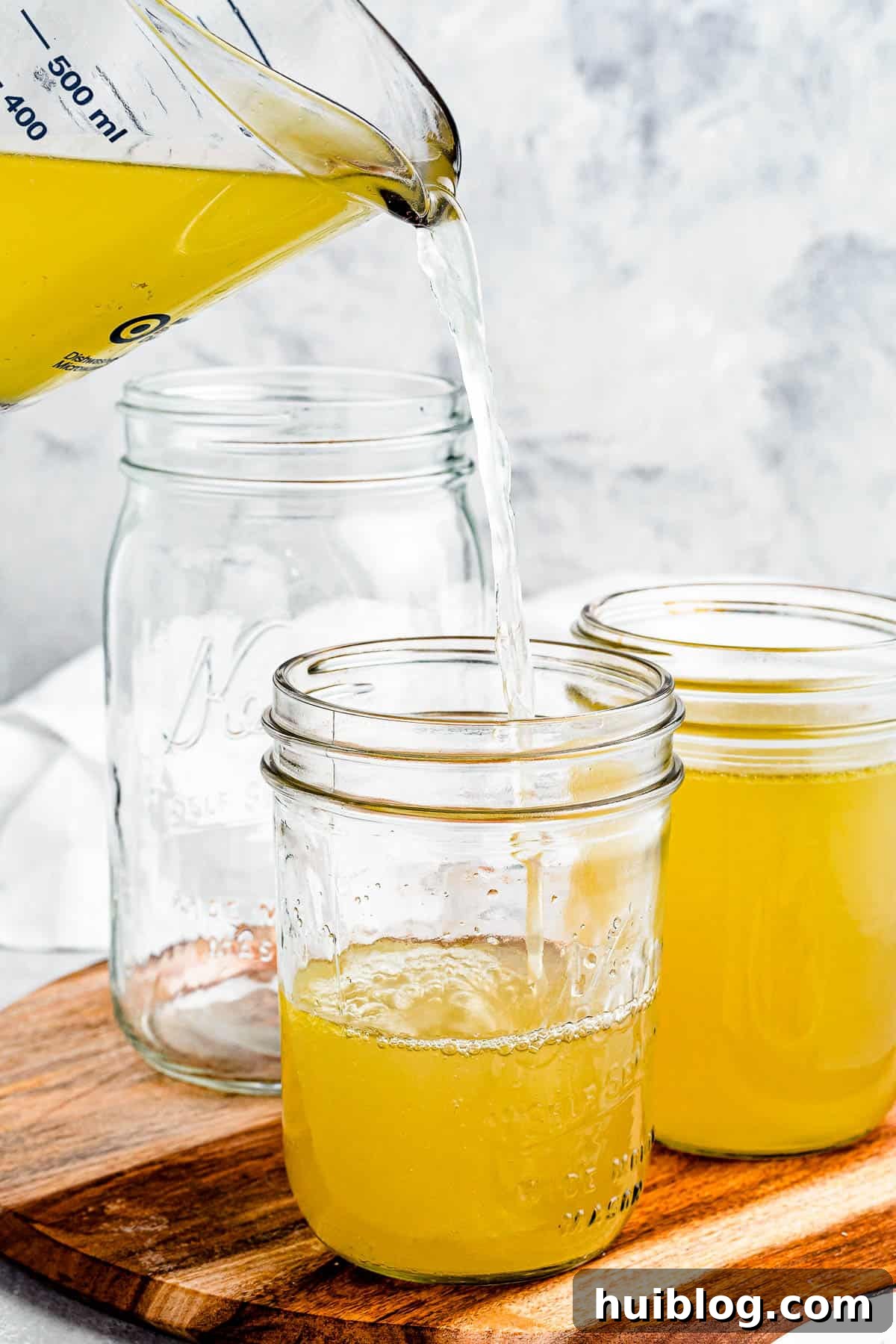 Liquid Gold: Instant Pot Chicken Broth 3 Chicken broth being poured from a large measuring cup into several jars, showcasing the rich golden color and clarity of homemade broth.