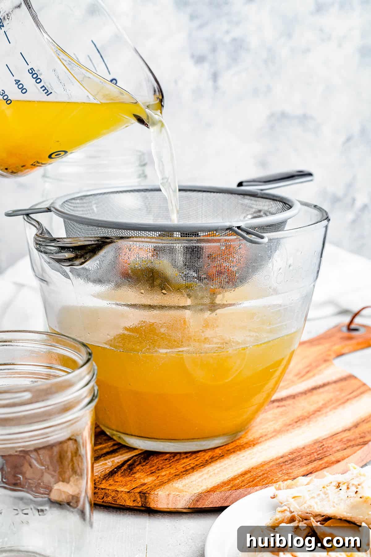 Liquid Gold: Instant Pot Chicken Broth 6 Rich chicken broth being carefully poured from a large measuring cup into a bowl through a fine-mesh sieve, ensuring a clear and smooth finished product.