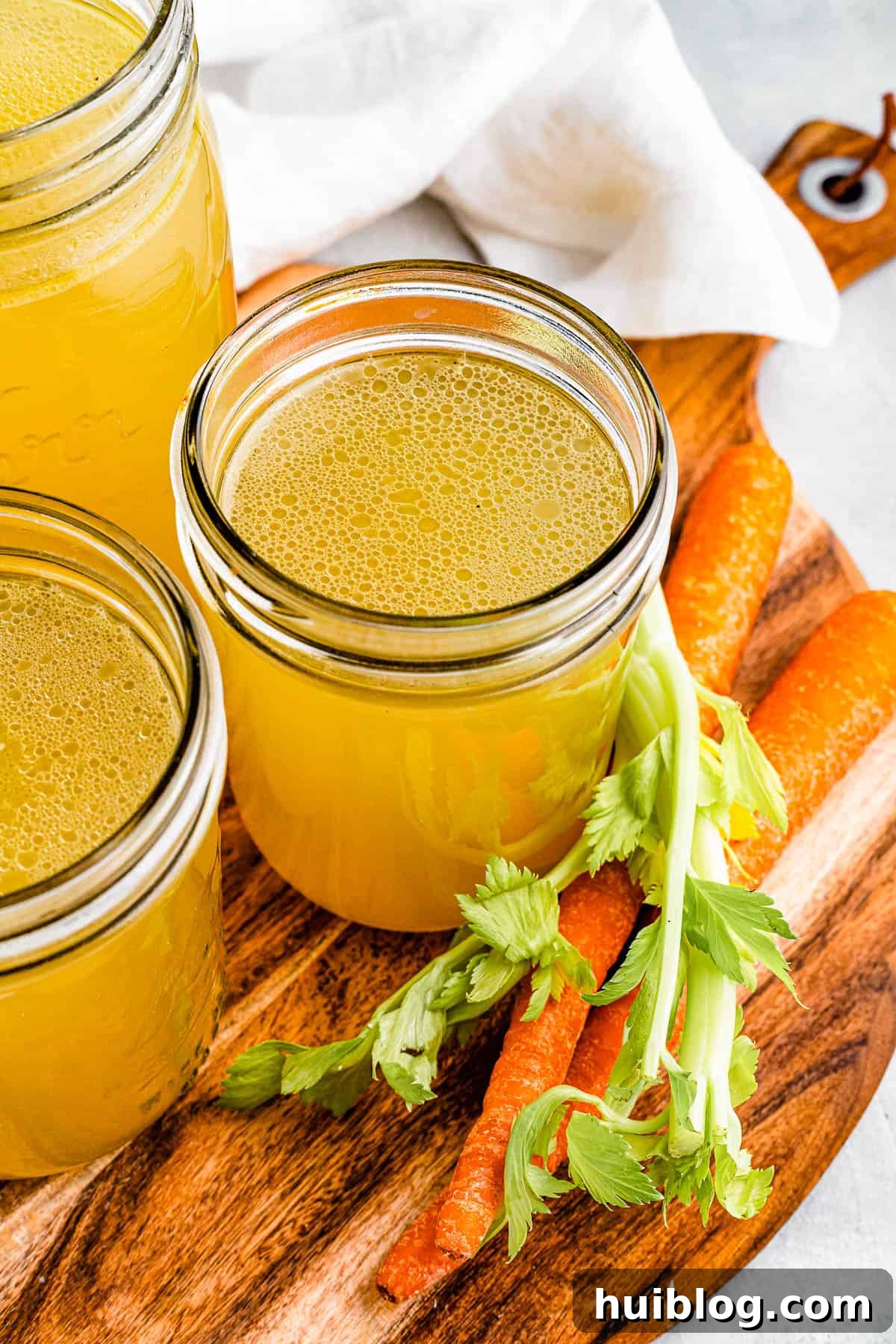 Liquid Gold: Instant Pot Chicken Broth 8 Three jars of chicken broth on a cutting board with raw carrots nearby, symbolizing the wholesome ingredients used to create this nourishing liquid.
