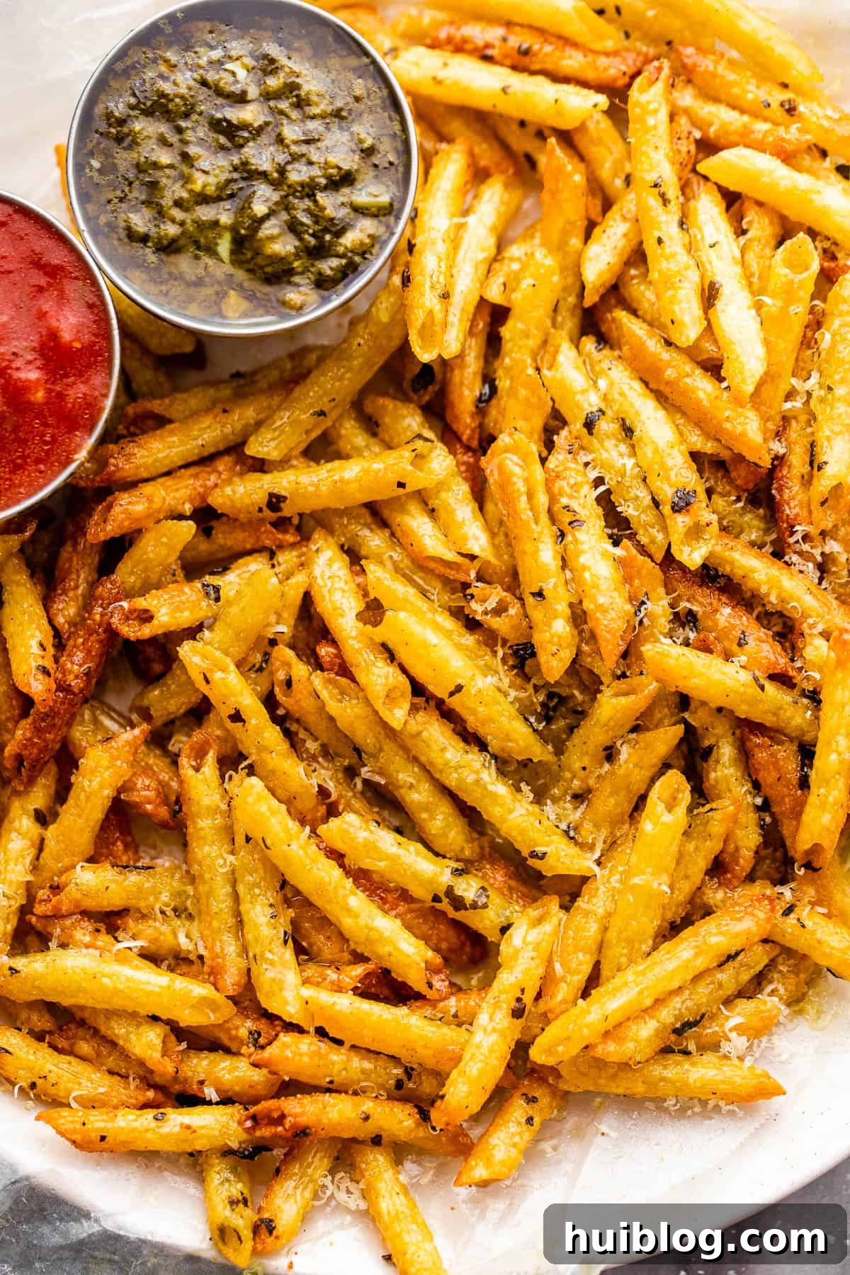 A vibrant plate of golden-brown pasta chips, artfully arranged and served with side dishes of rich basil pesto and classic marinara sauce, inviting you to dip and enjoy.
