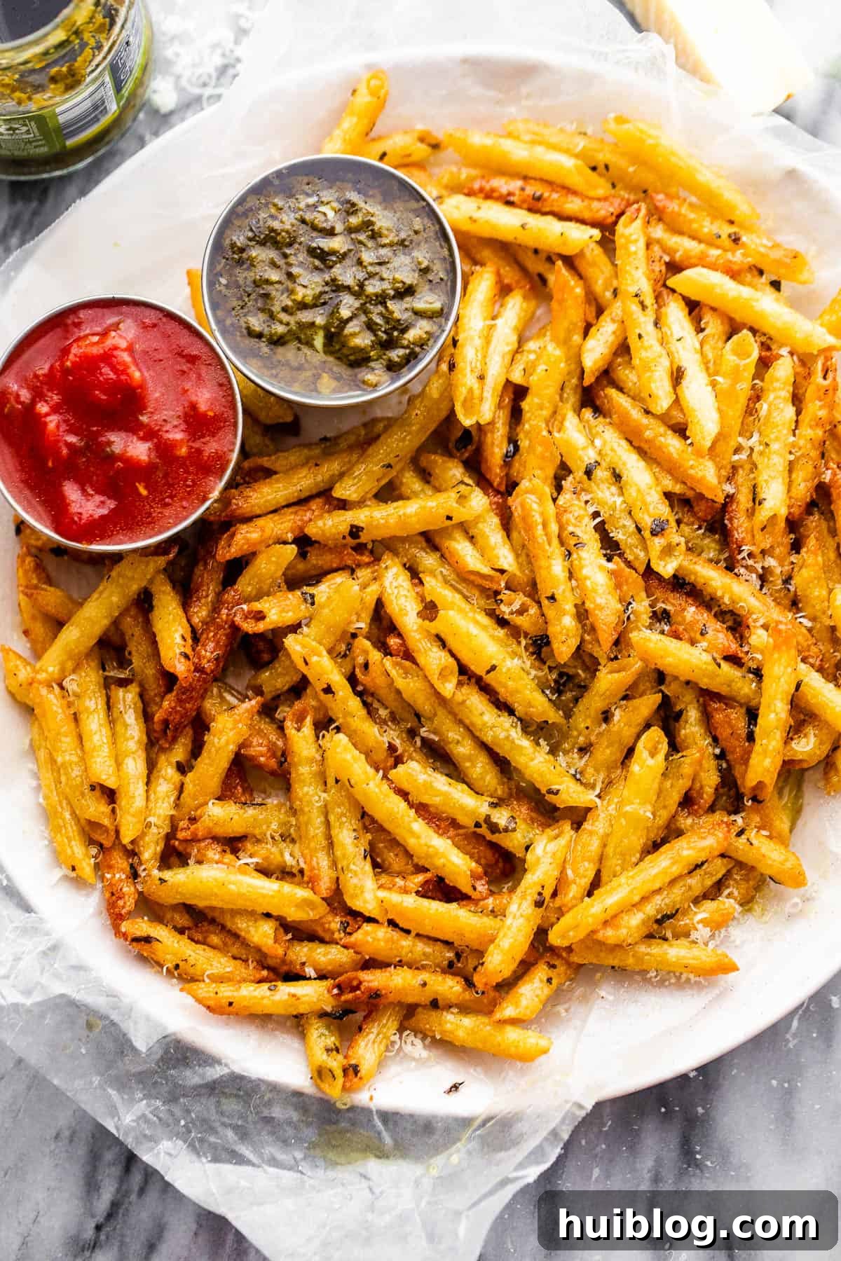 A close-up shot of a plate laden with beautifully baked pasta chips, ready to be enjoyed with small bowls of vibrant green basil pesto and rich red marinara sauce, perfect for dipping.