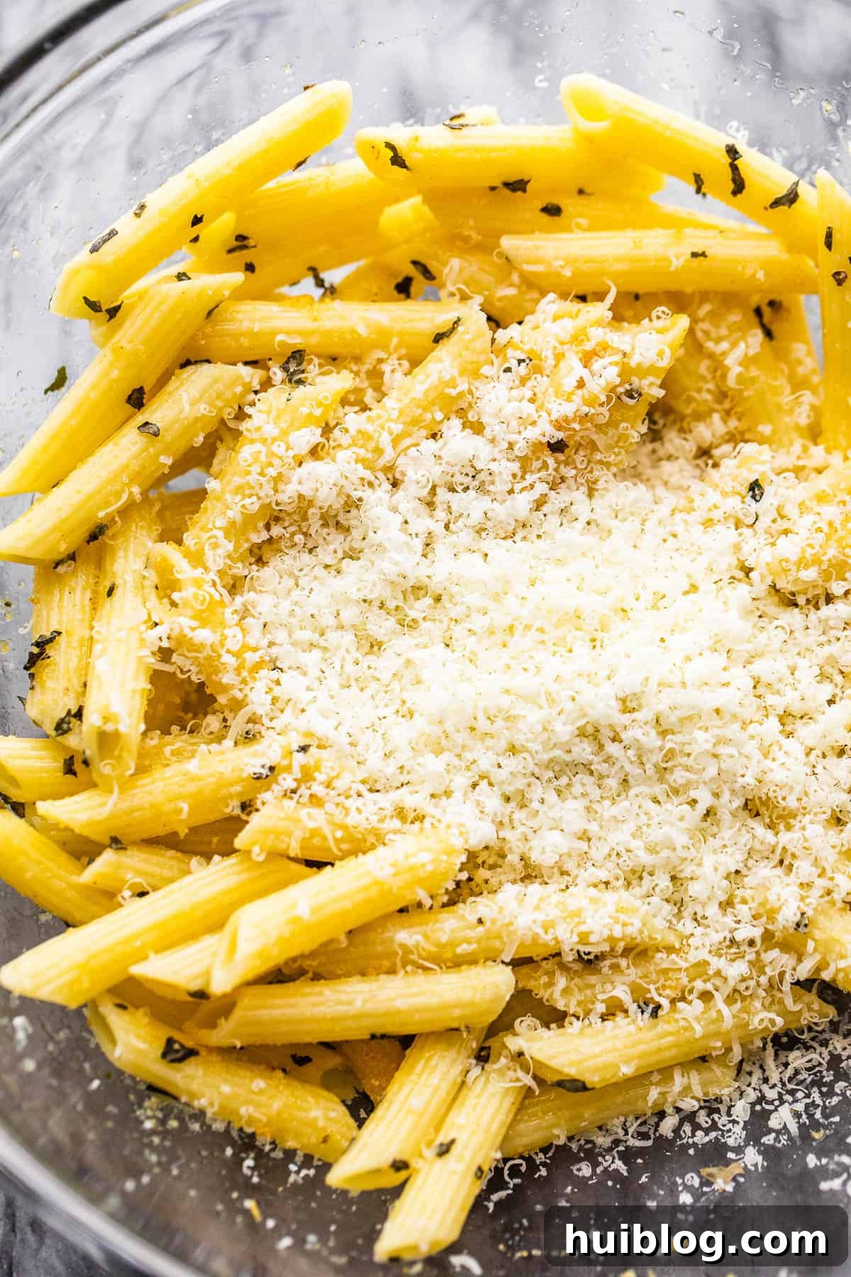 A bowl filled with freshly boiled pasta, perfectly ready for the next step, with a generous mound of grated Parmesan cheese positioned in the center, awaiting to be mixed in.