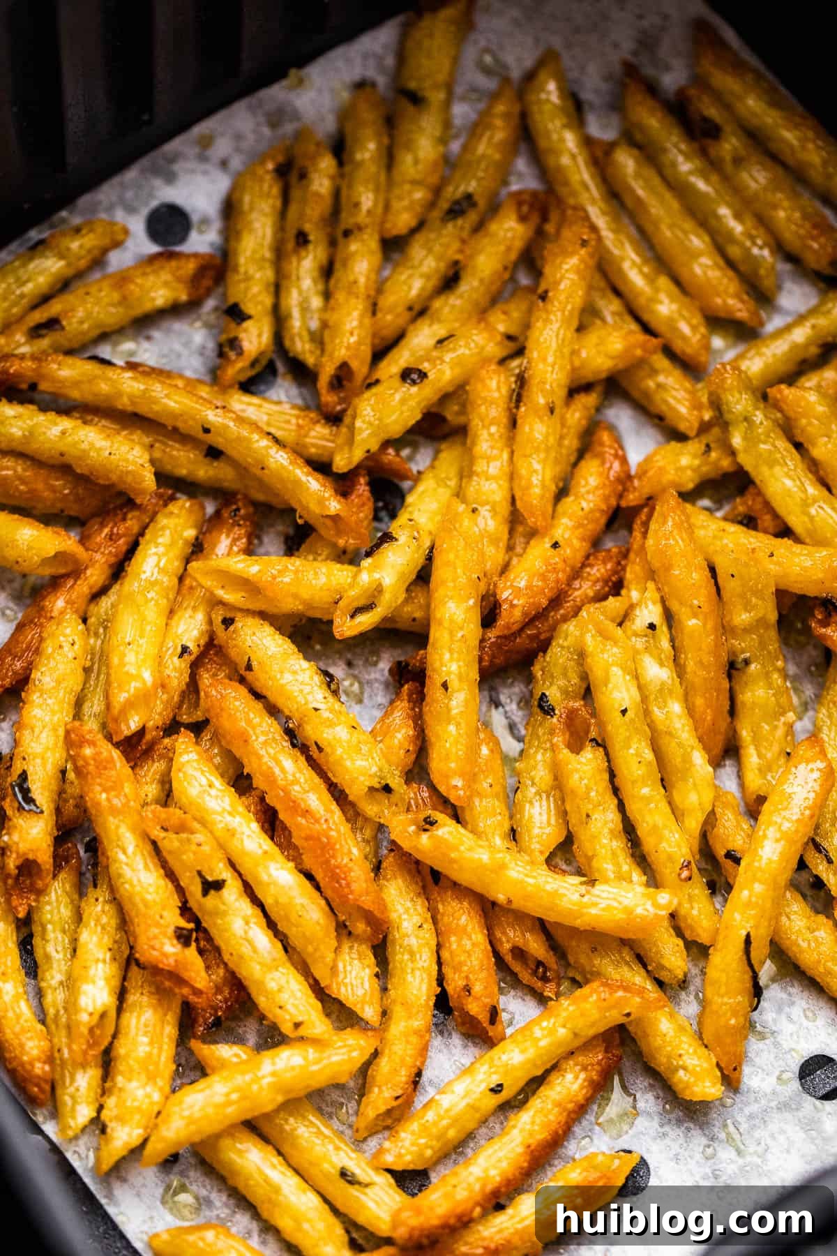 A close-up view of an air fryer basket filled with a freshly baked batch of golden, crispy pasta chips, hot and ready to be served.