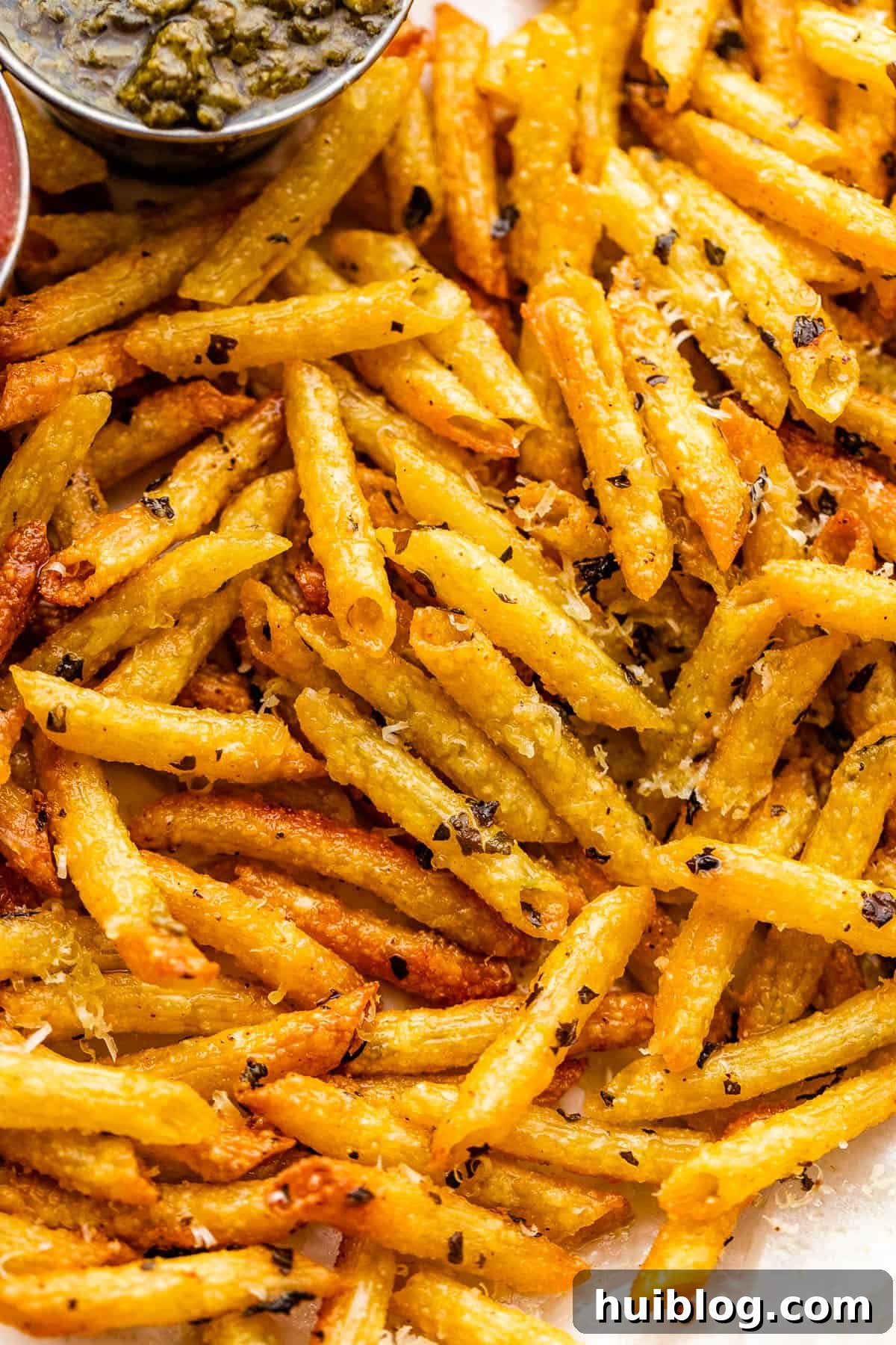 A close-up photo featuring golden-brown, crunchy pasta chips artfully arranged on a plate, with a small bowl of vibrant green basil pesto on the side, ready for dipping.