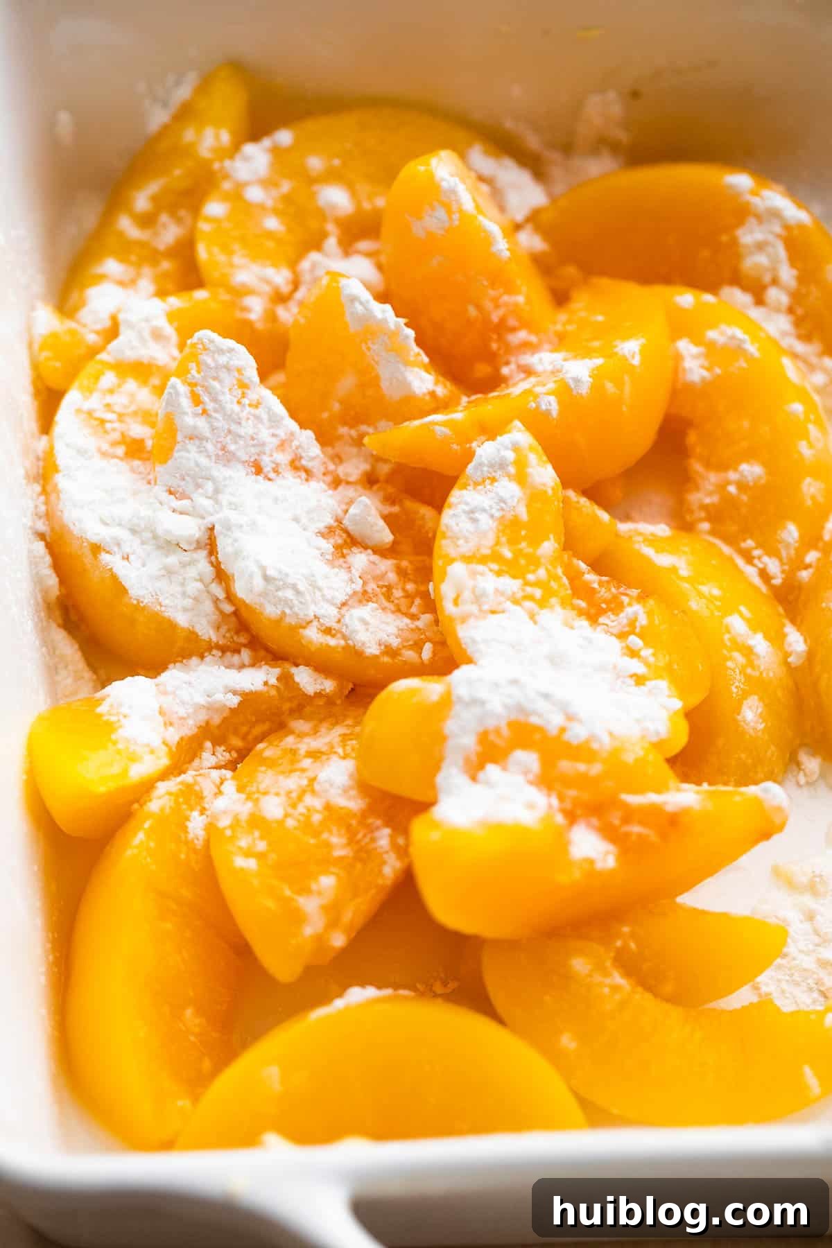 Freshly sliced peaches, gleaming and tossed with a light coating of cornstarch and sugar in a mixing bowl, ready for the baking dish.