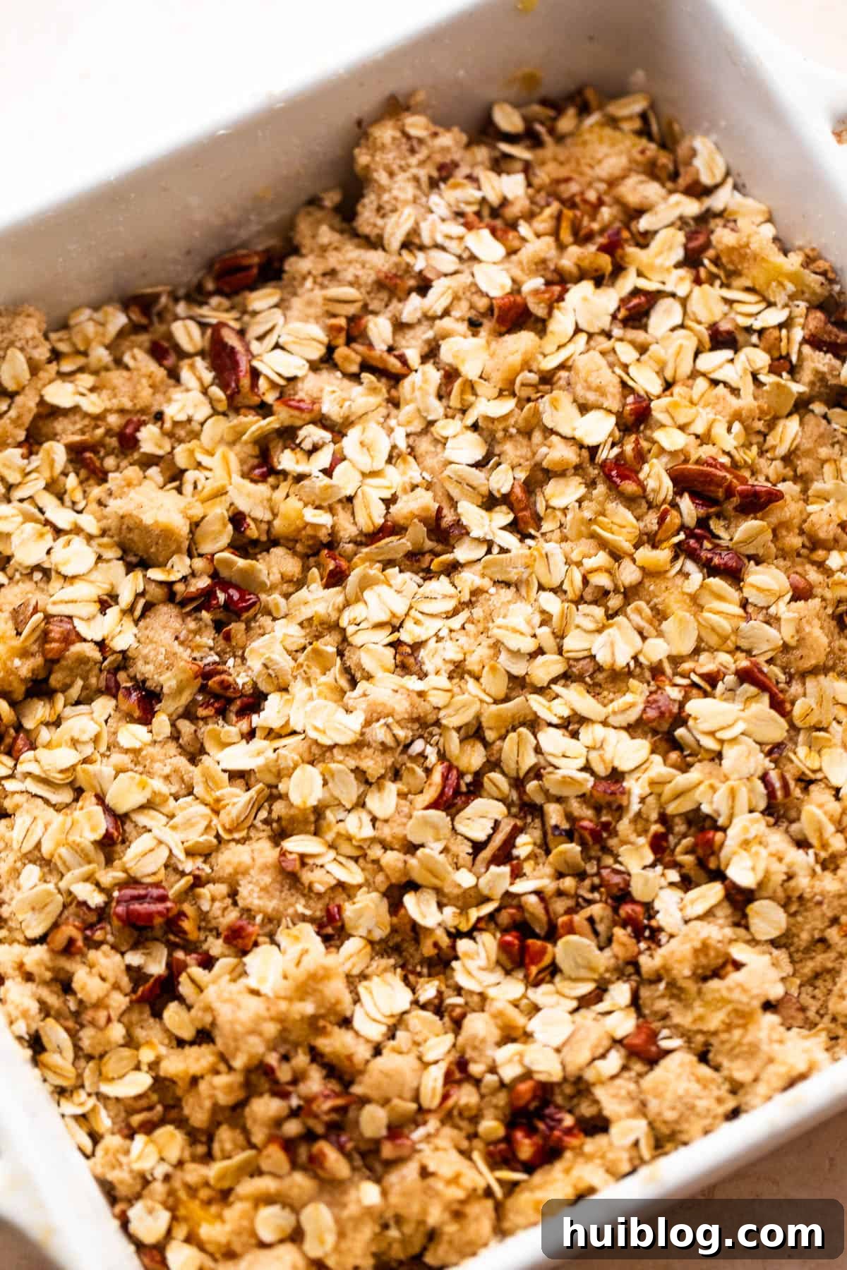 A squared baking dish showcasing a peach crisp, with the golden-brown topping of oats, flour, and pecans evenly spread over the succulent peach slices.