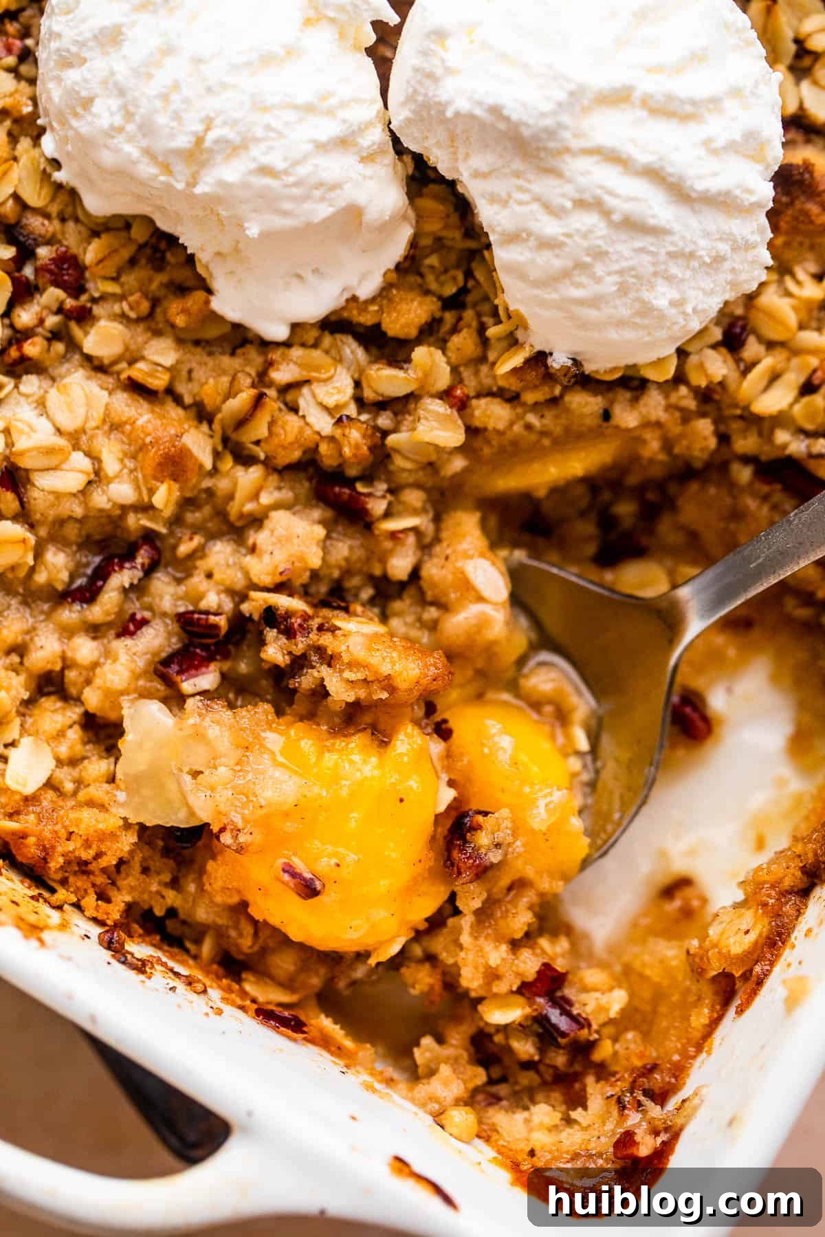 A beautiful peach crisp in a white ceramic baking dish, topped with multiple scoops of creamy vanilla ice cream, creating a delightful visual of warm and cold.