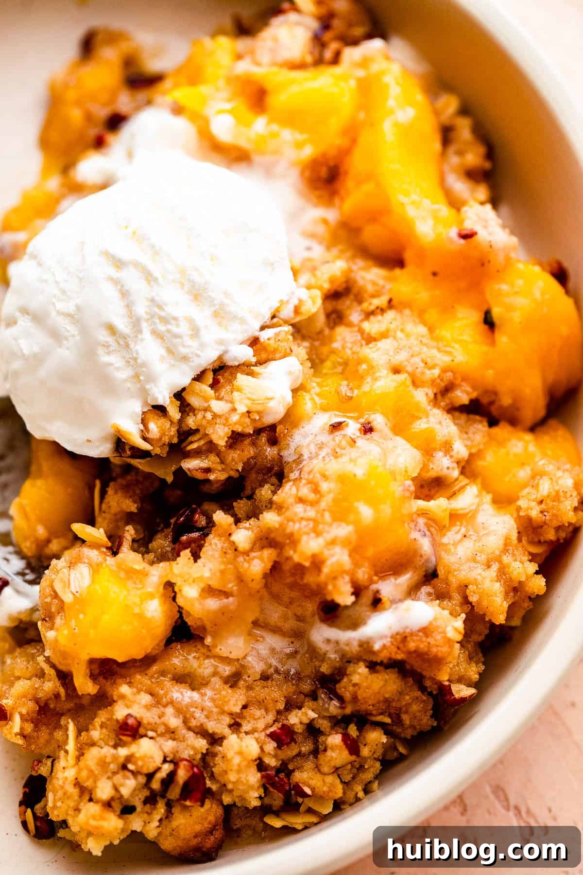A comforting bowl of warm peach crisp, generously topped with a single scoop of melting vanilla ice cream, creating a perfect dessert.