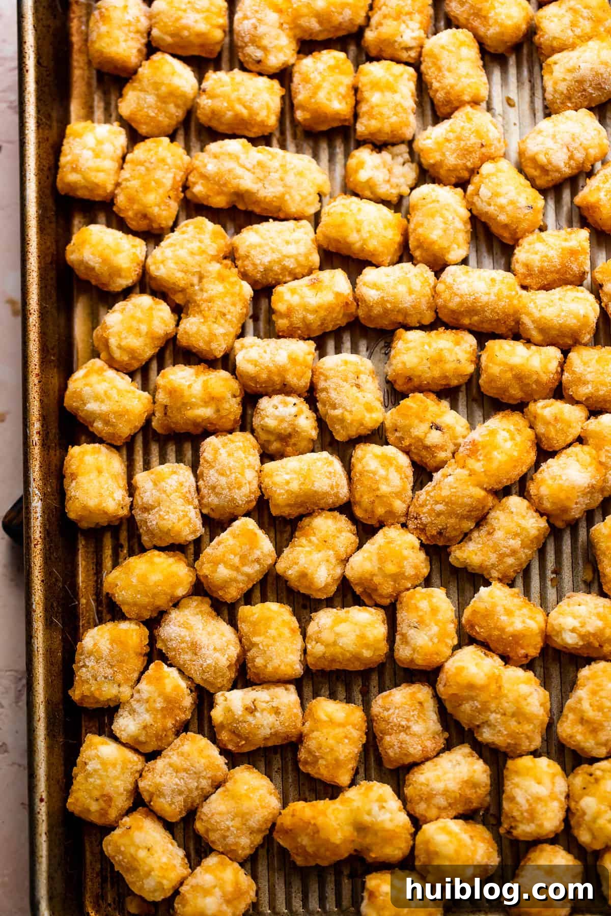 Loaded Sheet Pan Beef Totchos 4 A pristine sheet pan lined with parchment paper, evenly spread with a single layer of frozen tater tots, ready for baking to achieve optimal crispness.
