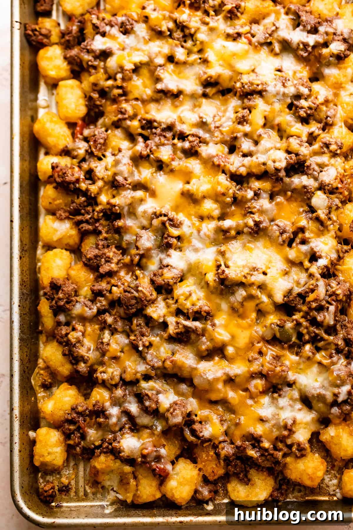 Loaded Sheet Pan Beef Totchos 5 A baking sheet laden with freshly baked tater tots, generously covered with seasoned ground beef and a thick layer of perfectly melted golden-brown cheese, highlighting the delicious layers of the totchos.