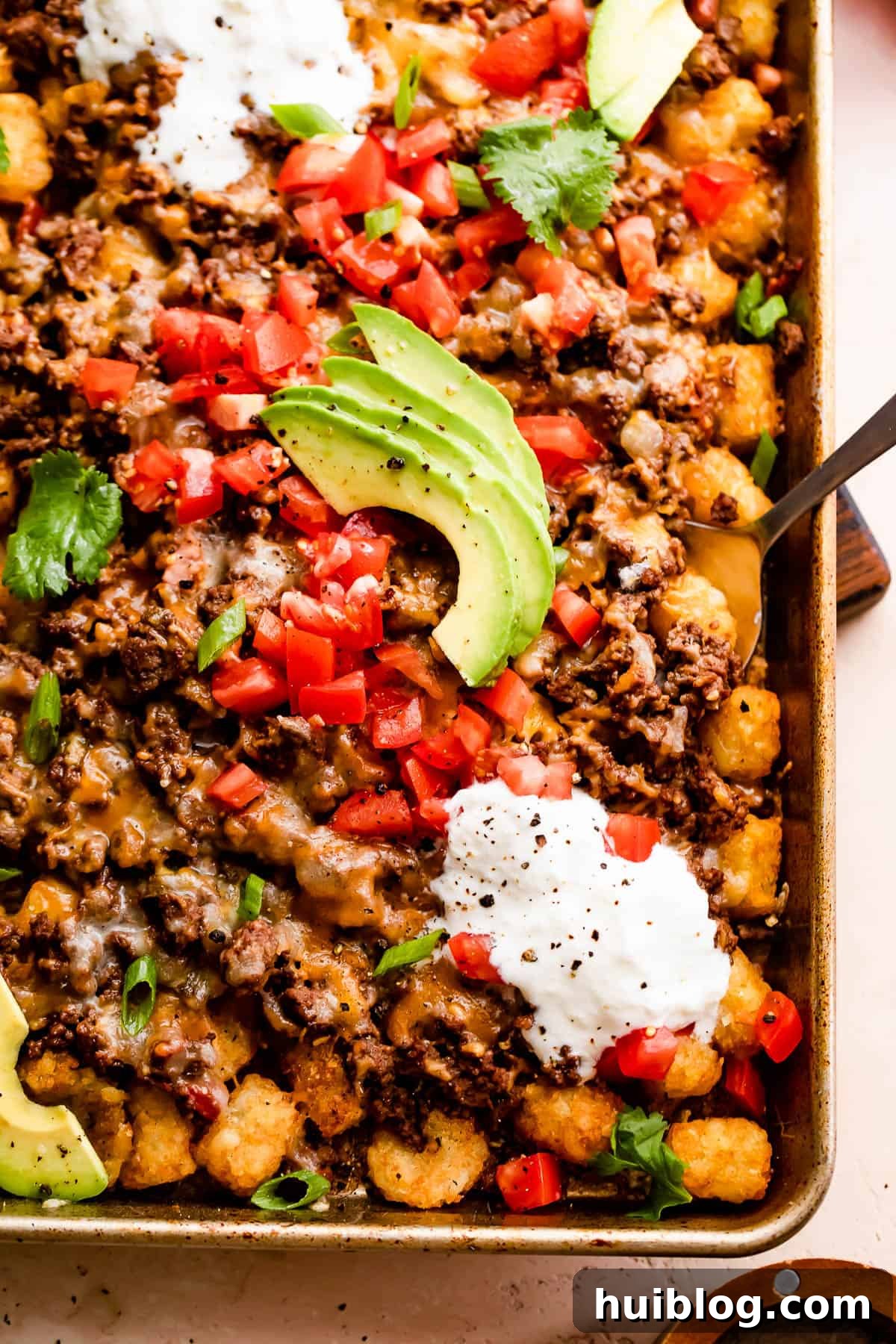 Loaded Sheet Pan Beef Totchos 6 A vibrant and fully loaded sheet pan of totchos, showcasing crispy tater tots, savory ground beef, generously melted cheese, fresh diced tomatoes, creamy sour cream, and vibrant avocado slices, ready to be enjoyed.