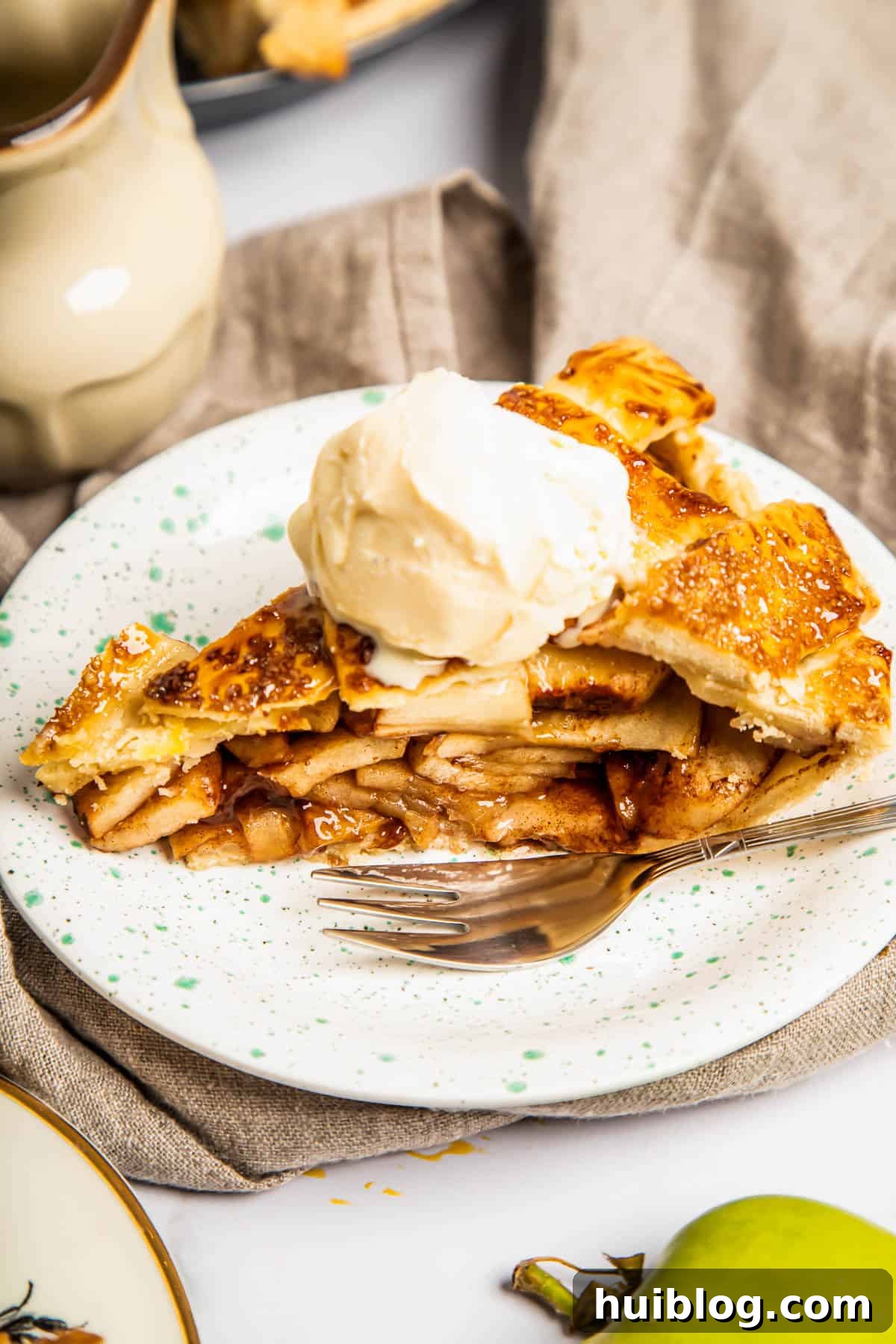 a slice of apple pie topped with ice cream on a plate with a fork