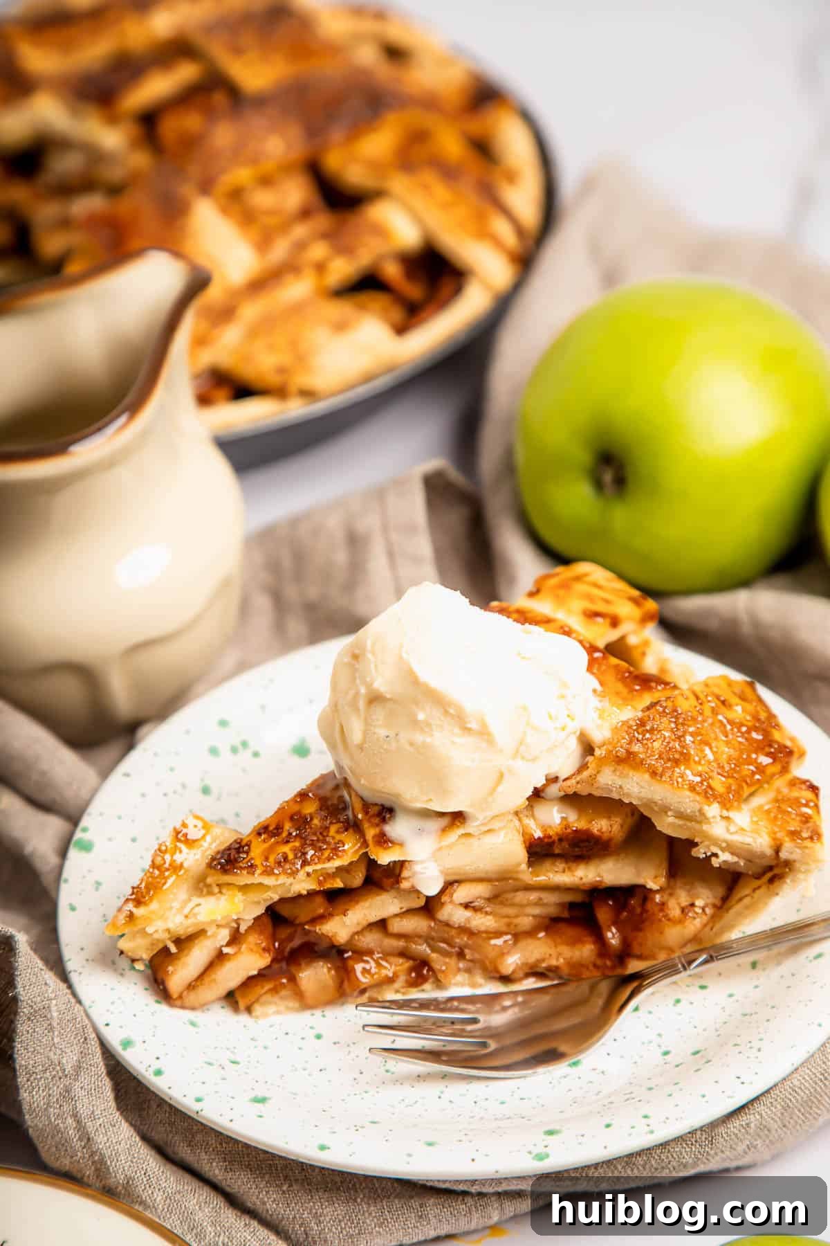 a slice of apple pie topped with ice cream on a plate with a fork