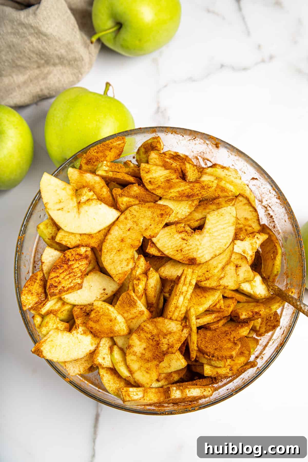 Thinly sliced apples coated with sugar, spices, and cornstarch in a large mixing bowl, ready to be transferred to the pie crust.