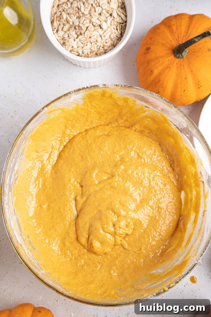A bowl filled with rich, orange pumpkin muffin batter, ready for baking.
