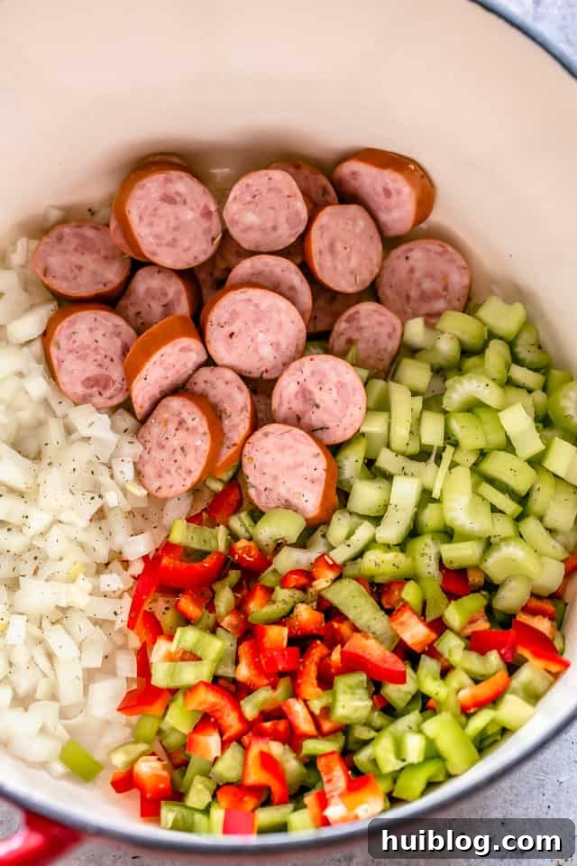 Diced onions, celery, and bell peppers, alongside sliced Andouille sausage, ready to be sautéed in a pot.