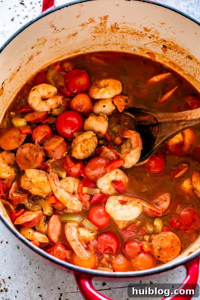 Chicken, Andouille sausage, and shrimp cooking together in a large pot, surrounded by a rich, bubbling sauce.