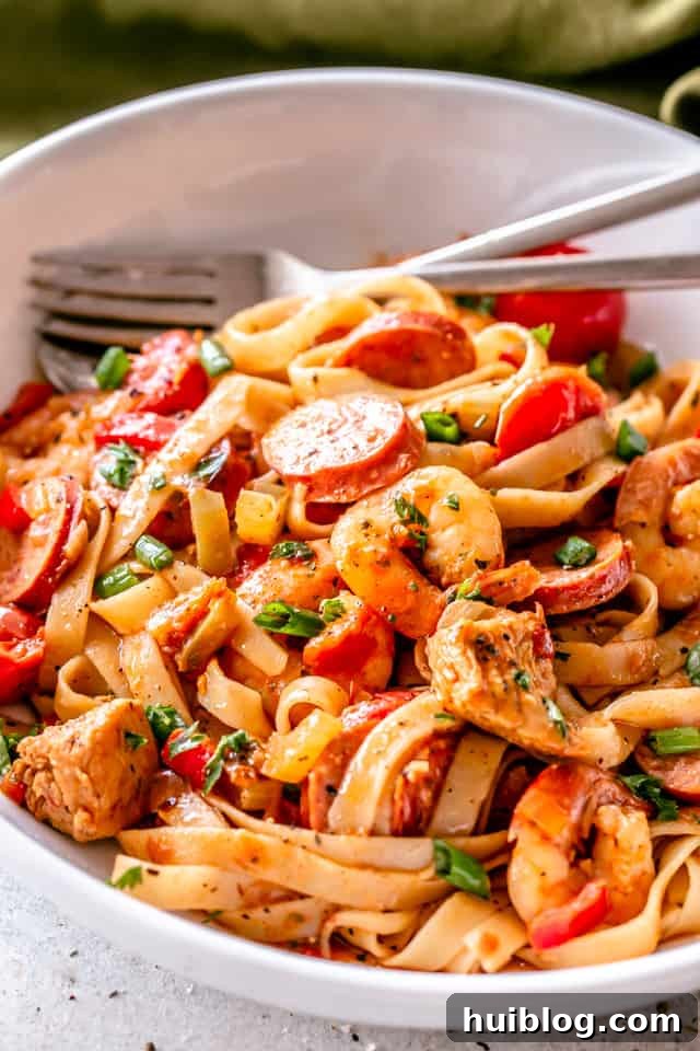 A vibrant close-up of One Pot Jambalaya Pasta in a white bowl, showcasing chicken, sausage, shrimp, and linguine.